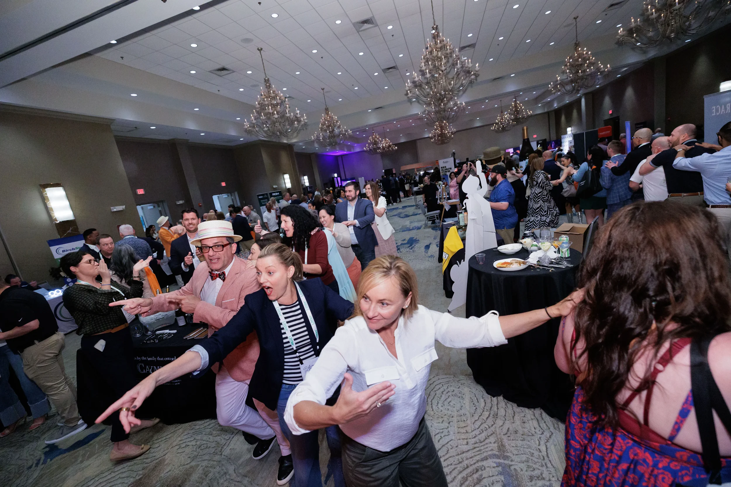 Large group of attendees dance and point at each other across Orlando corporate conference reception ballroom