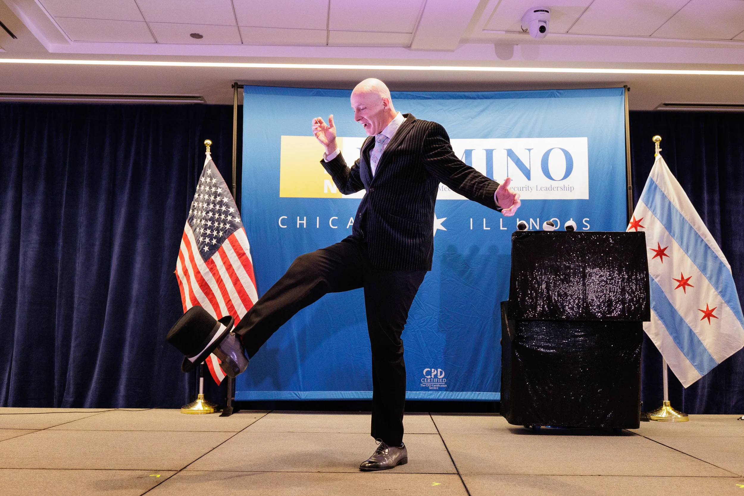 Entertainer kicks hat on branded stage beside Chicago flag at Orlando corporate conference evening event
