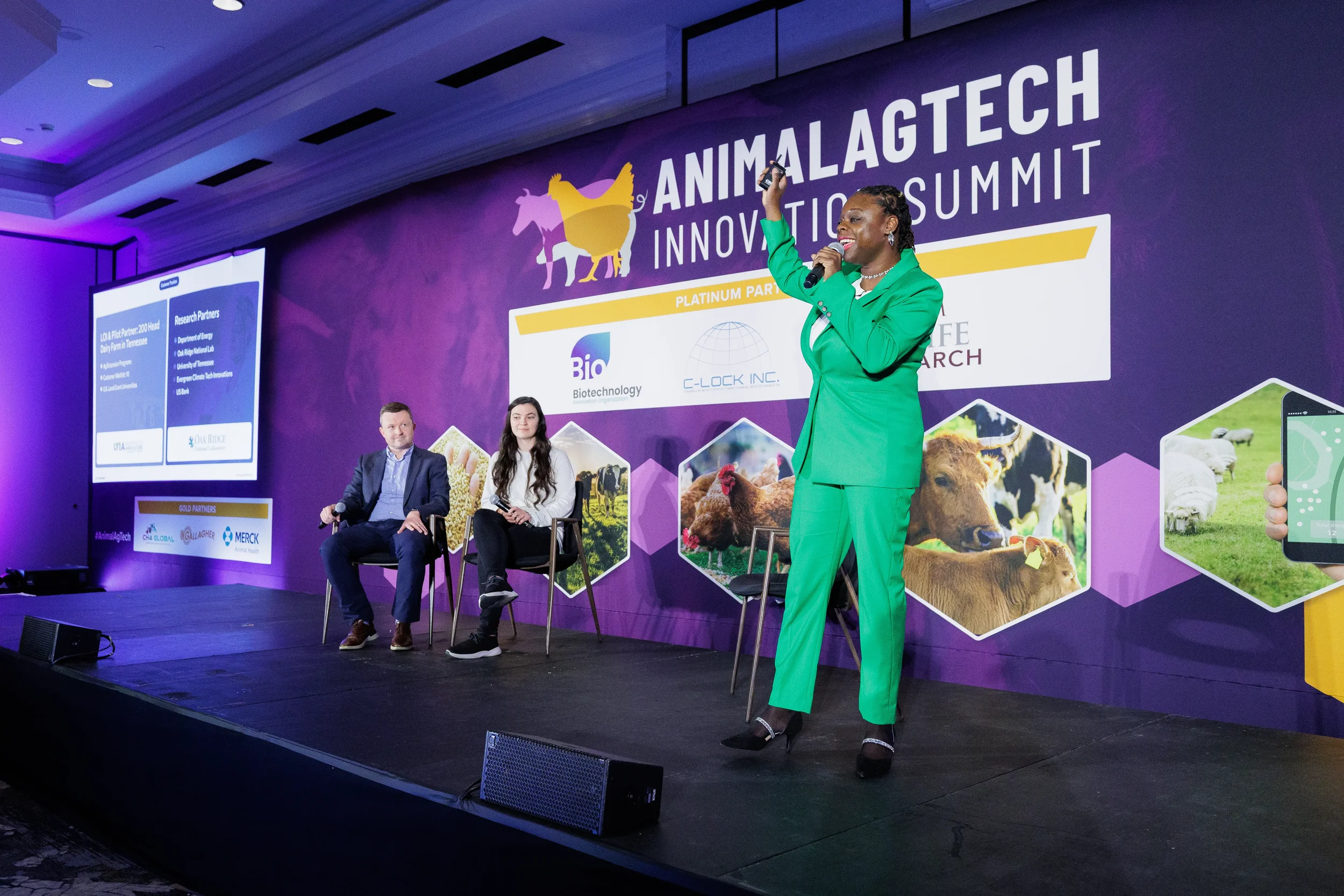 Speaker in green suit presents with microphone on branded stage at Orlando industry summit
