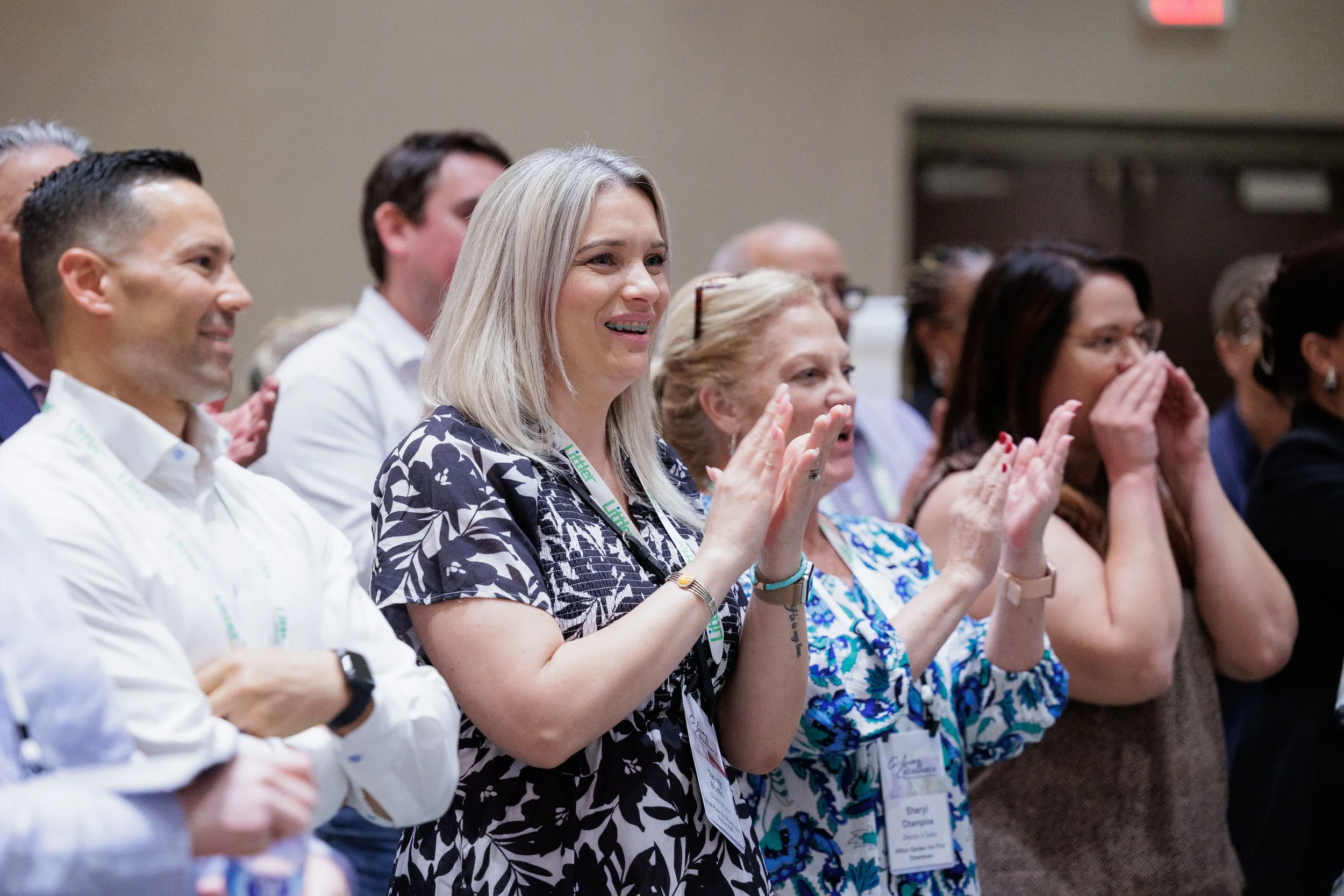Attendees with lanyards smile and applaud while standing in ballroom at Orlando industry conference