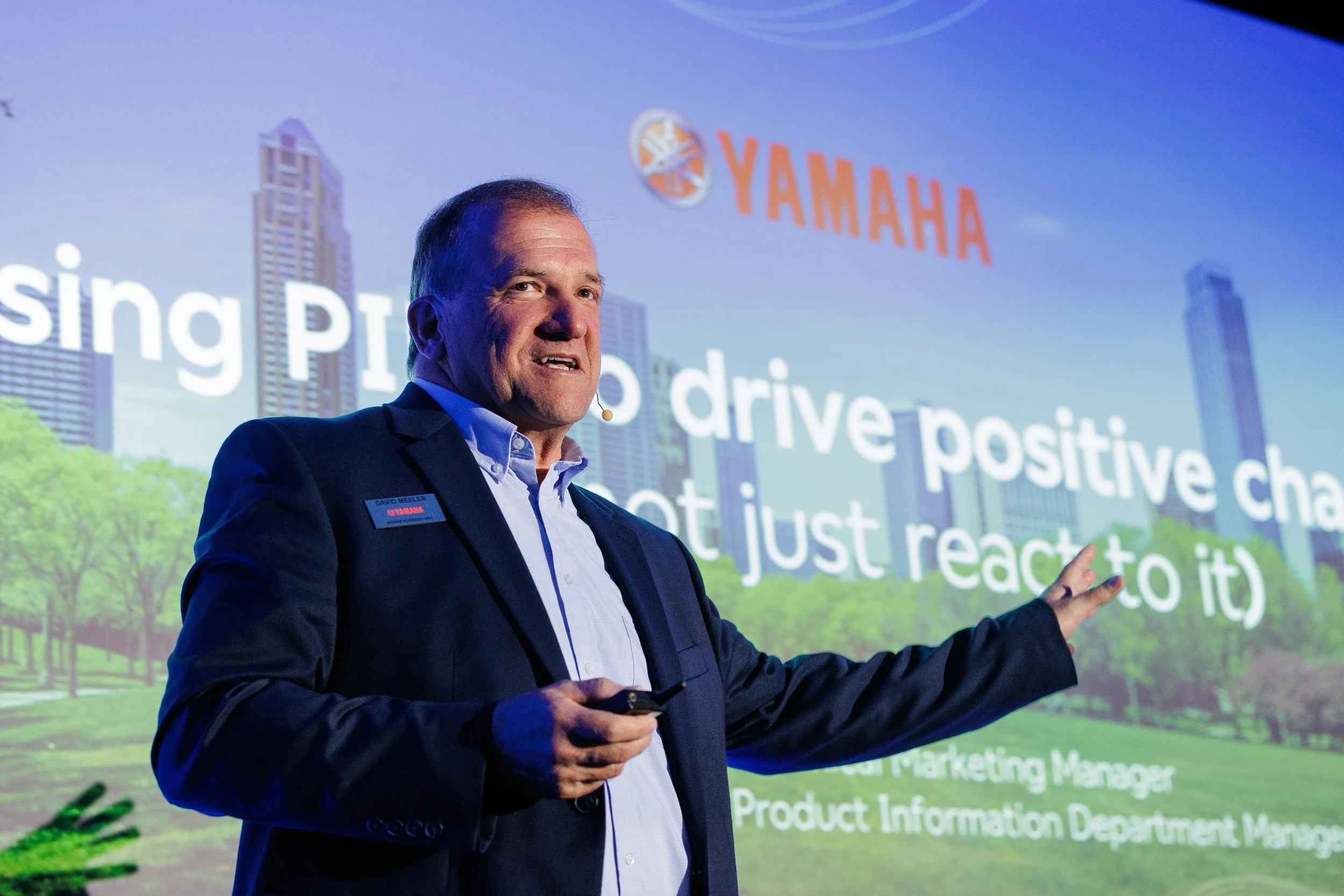 Speaker with headset microphone gestures toward large projection screen during Chicago industry conference