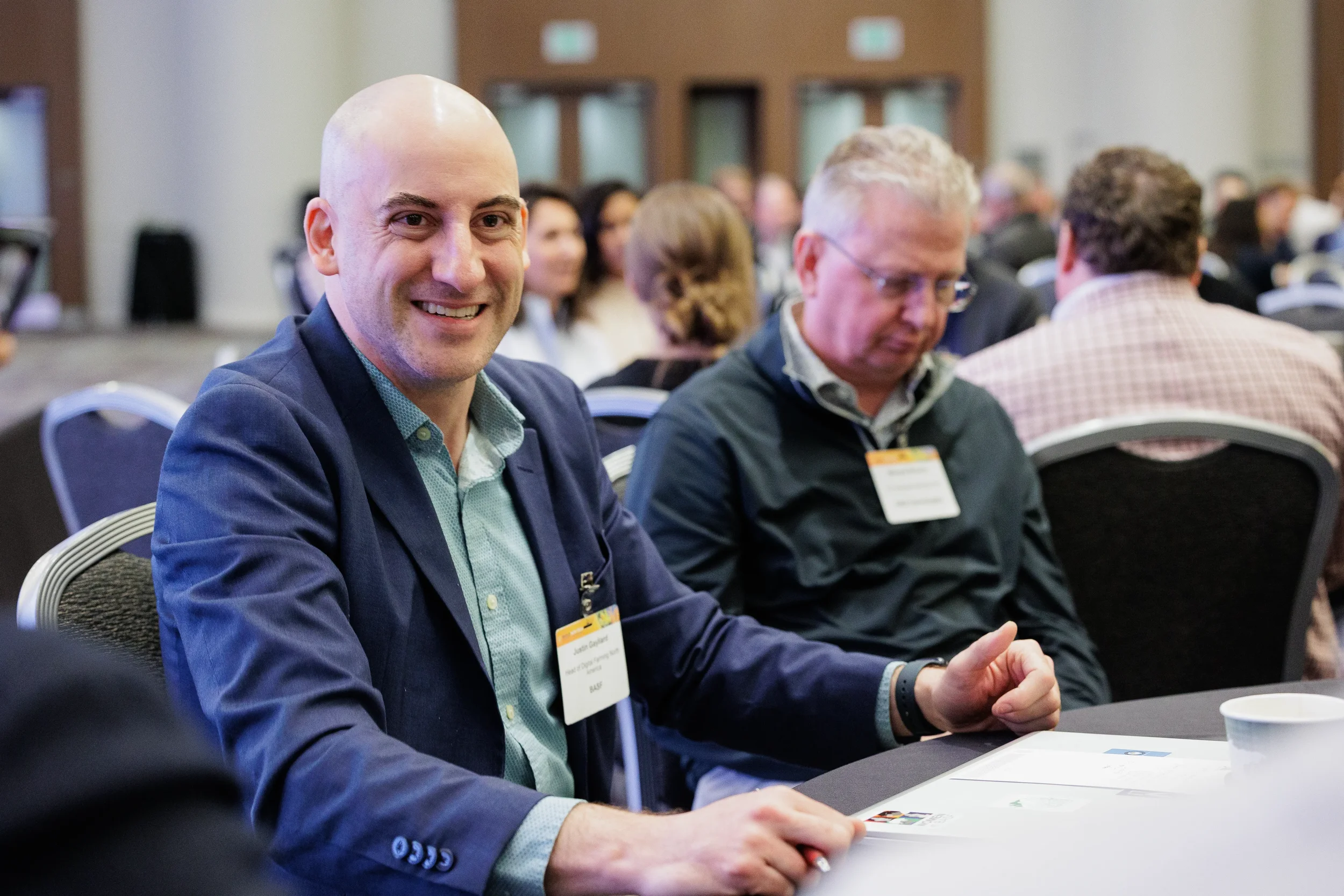 Smiling badged attendee seated at round table during session at Orlando industry conference