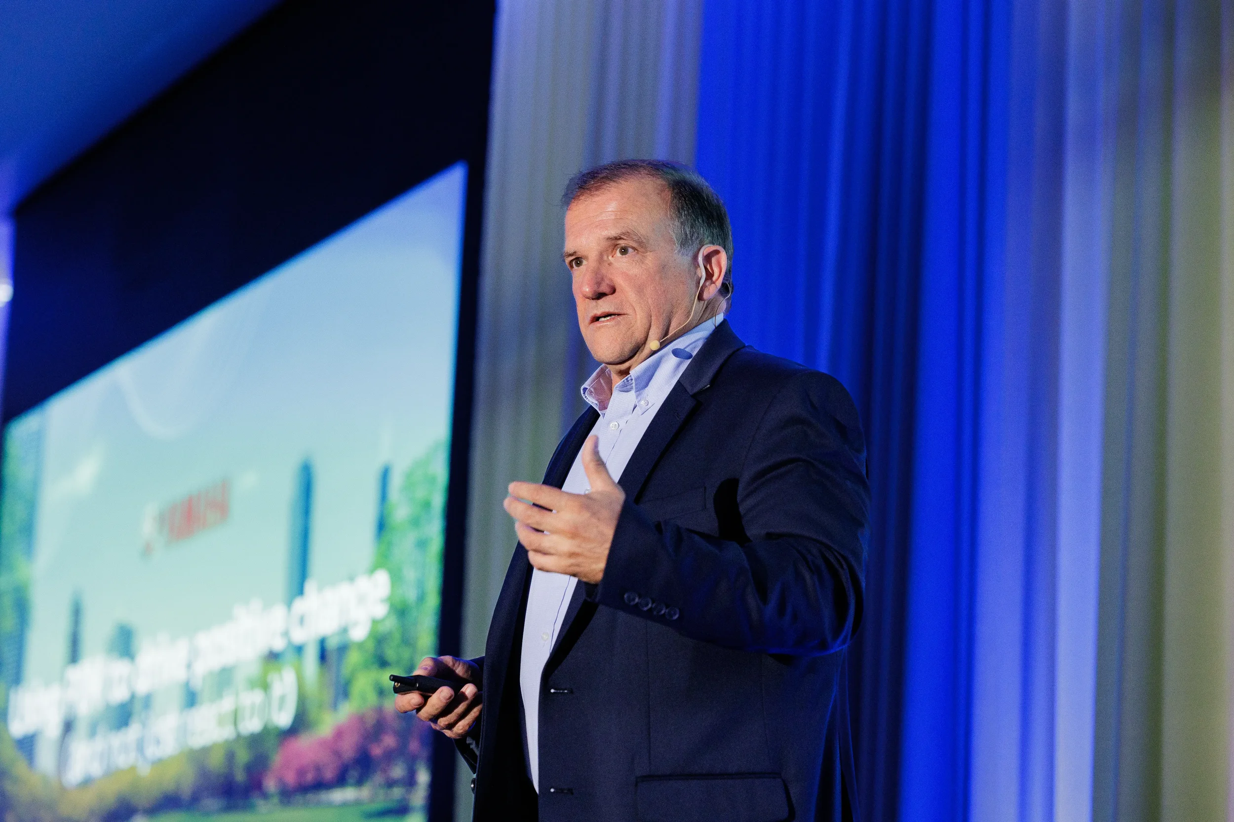 Speaker with headset microphone gestures on stage beside presentation screen at Orlando conference