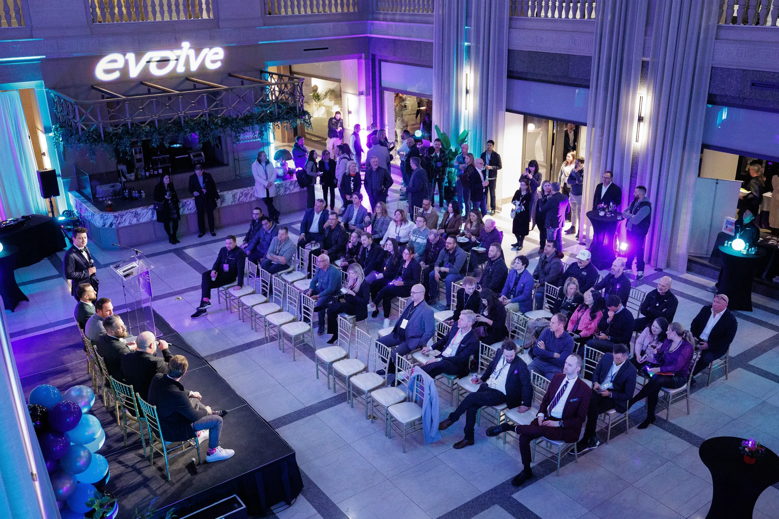 Overhead view of panel session on stage with full crowd seated in lit atrium at Chicago corporate event