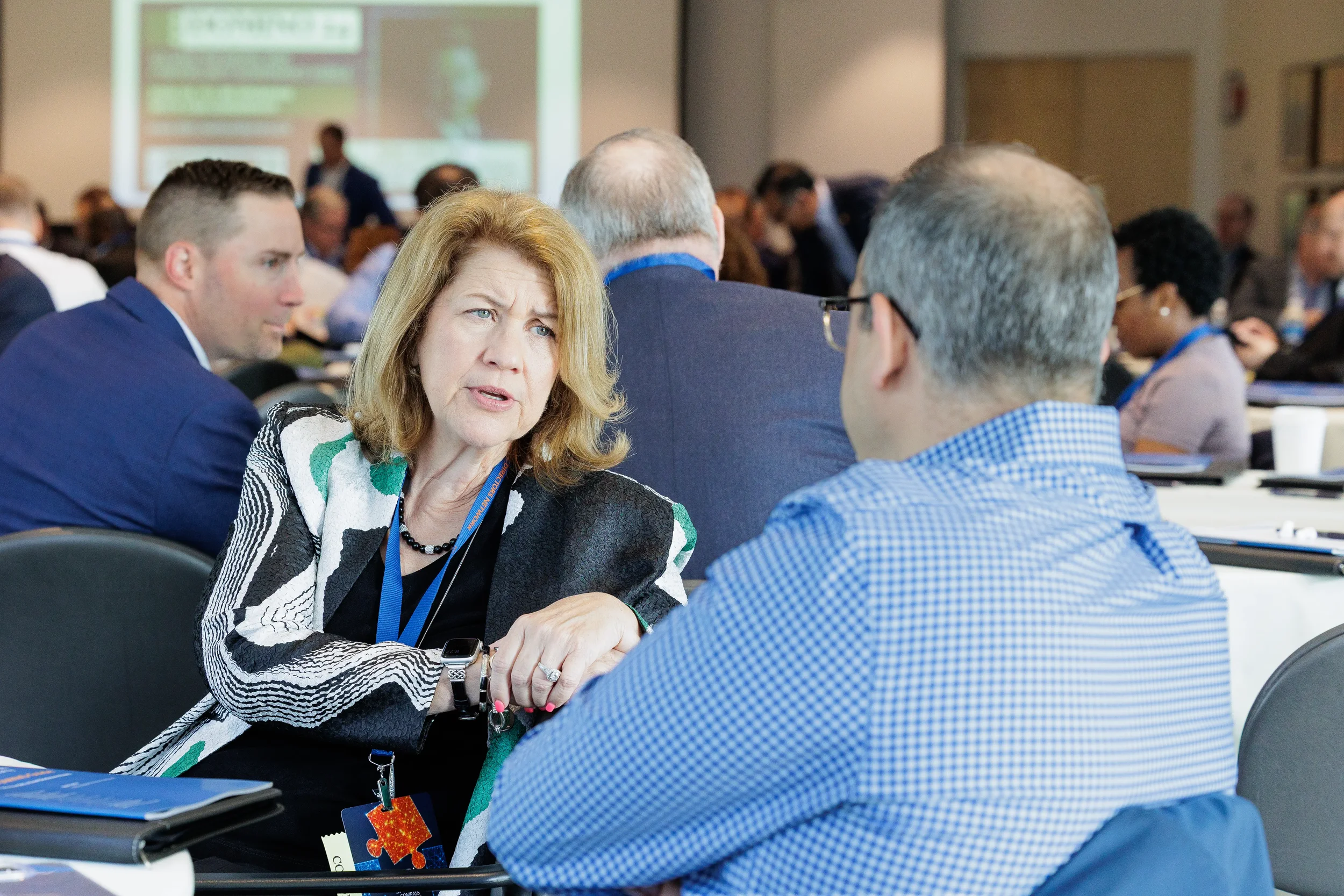 Female attendee with lanyard engages in animated conversation during seated Orlando industry conference session