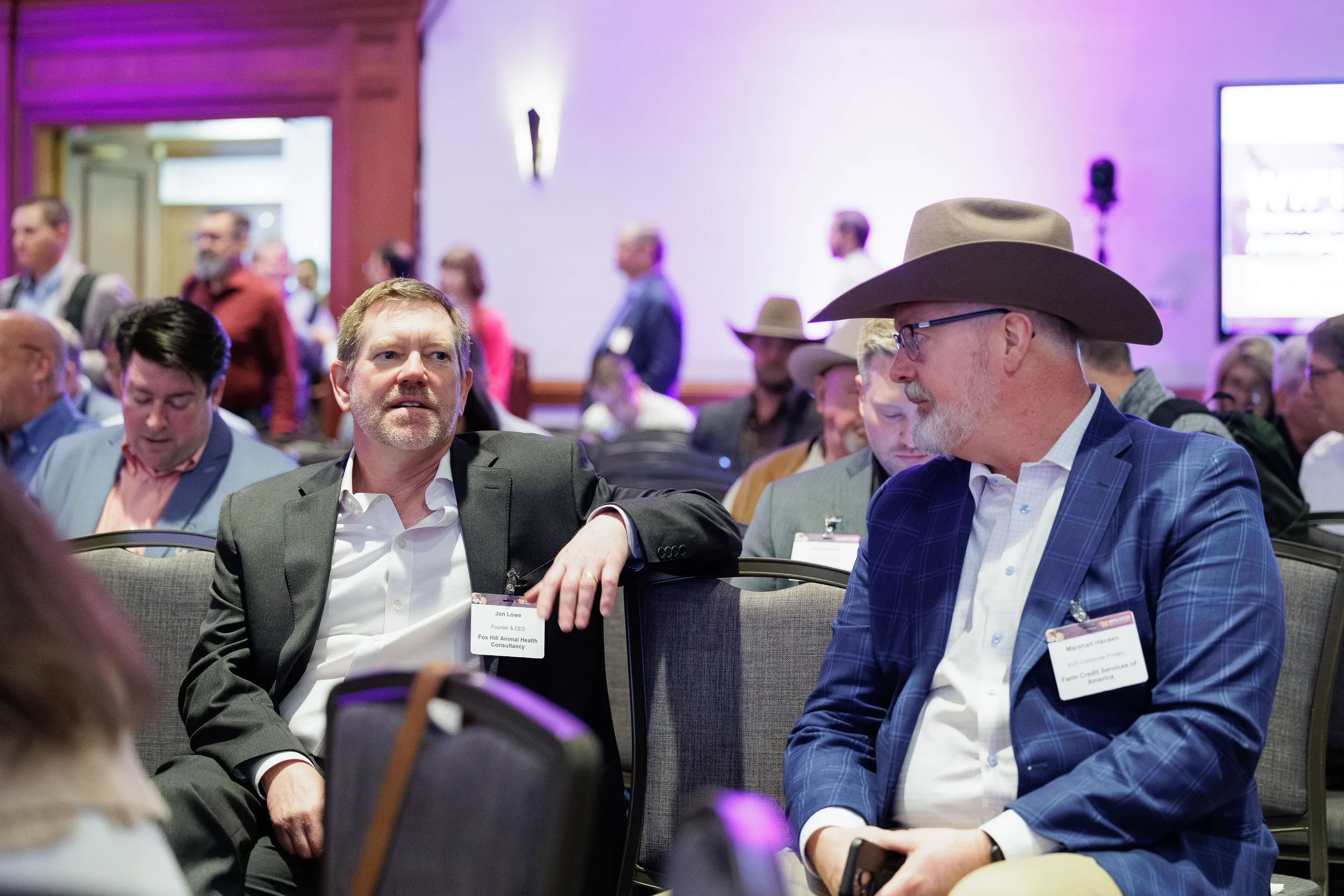 Two attendees converse in audience seating during session at Chicago industry conference