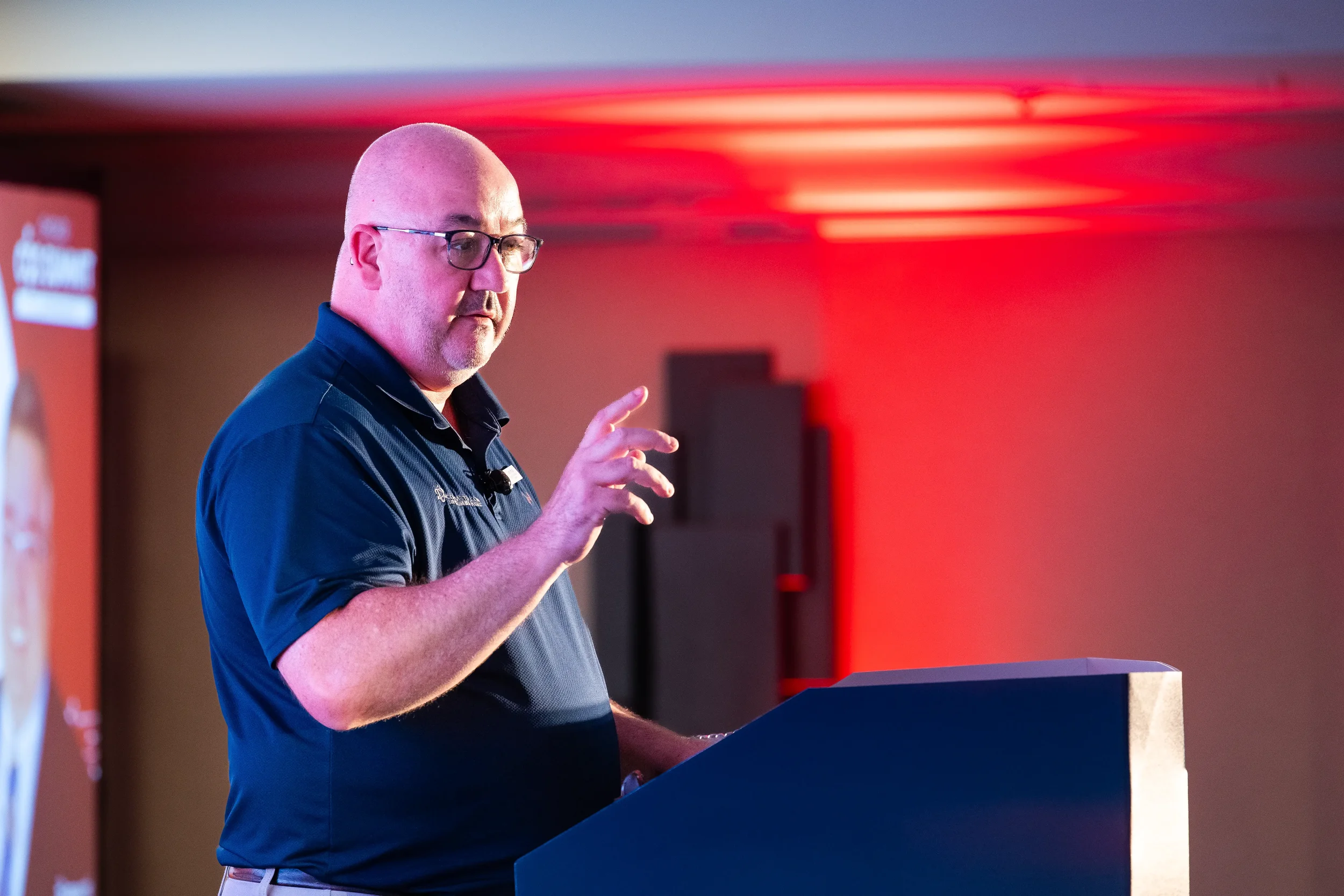 Speaker gestures while presenting from podium with dramatic red lighting at Chicago industry summit