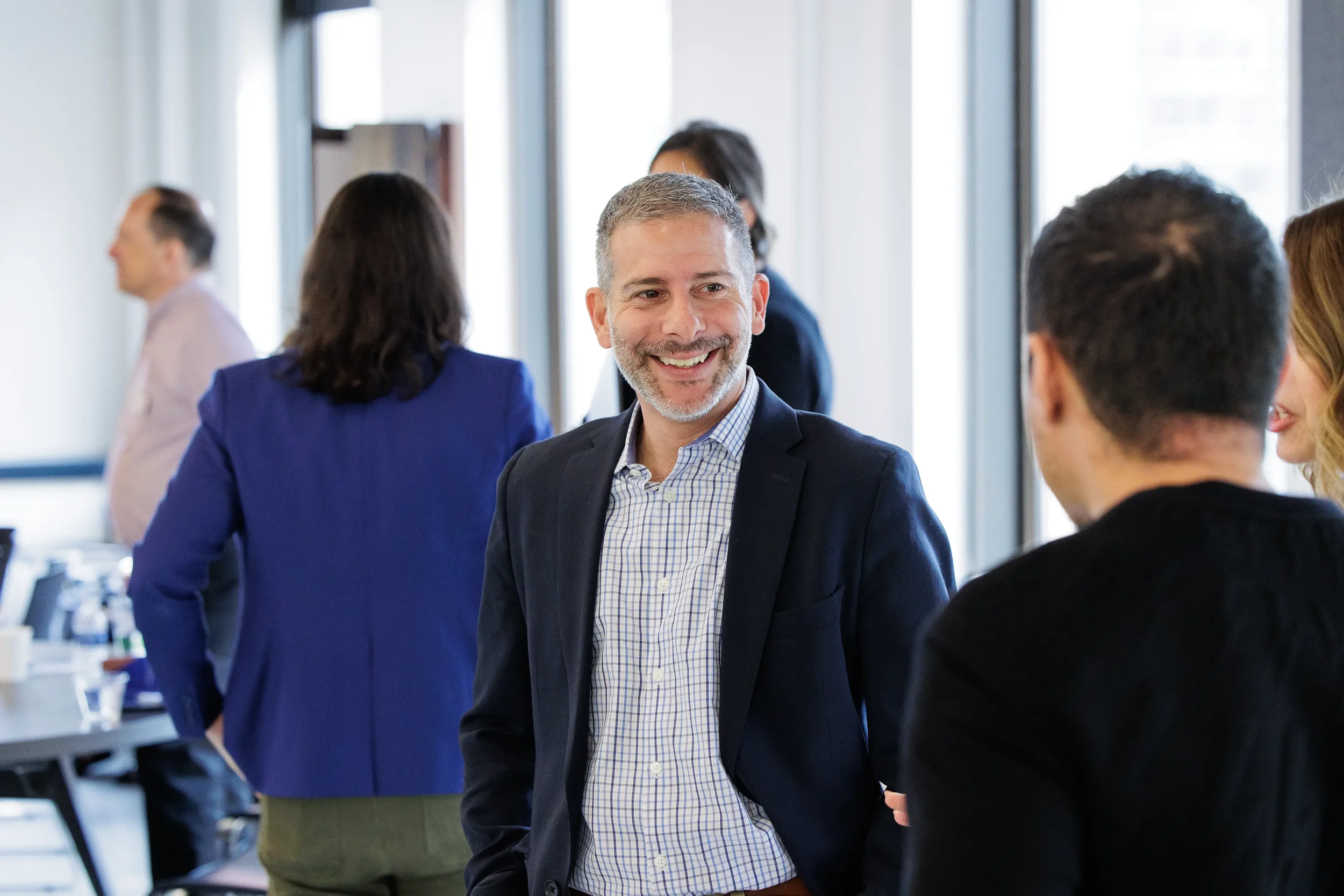 Male attendee smiles warmly while networking with others in bright venue at Orlando industry conference