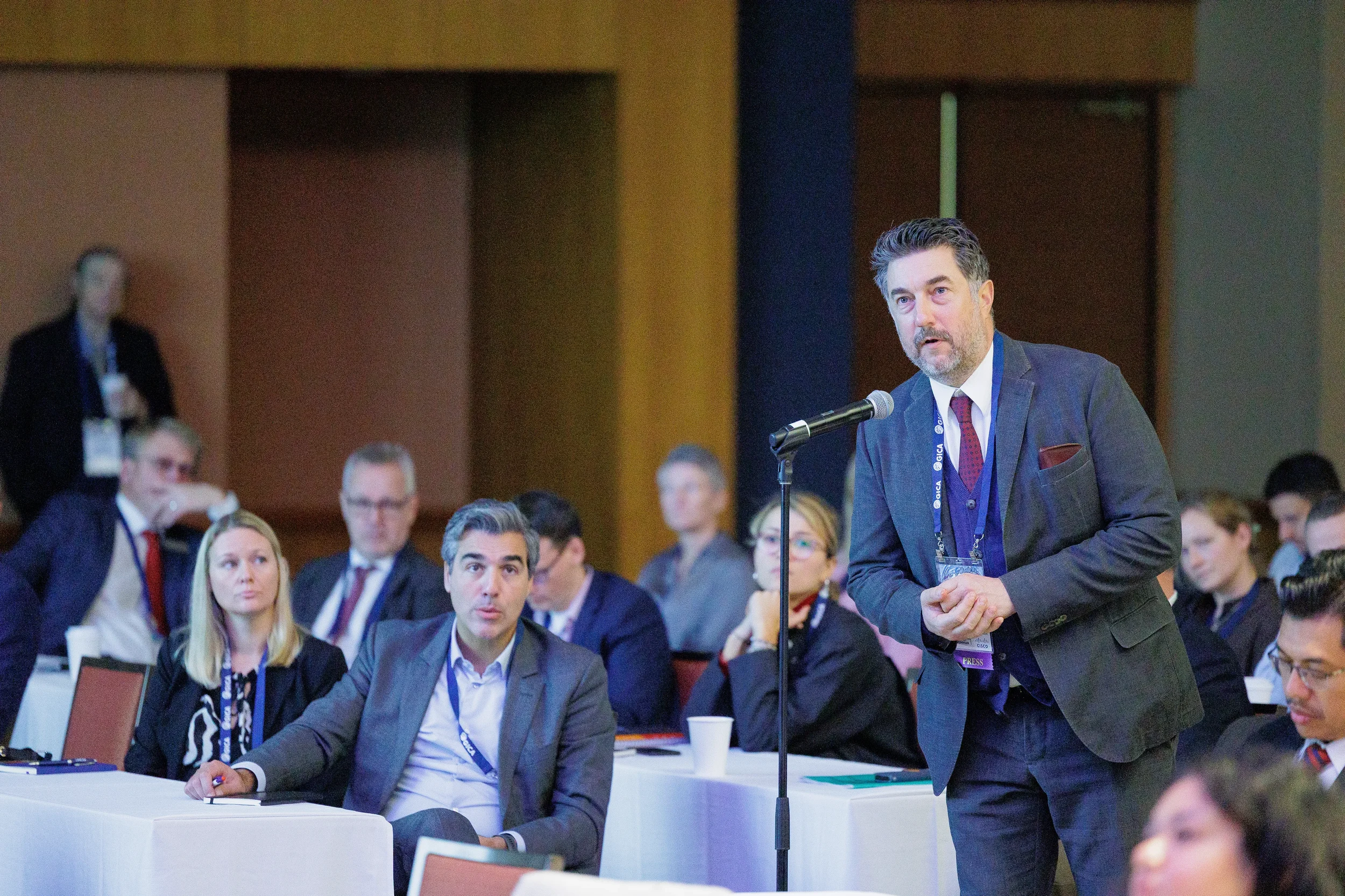 A well-dressed man speaks into a microphone stand, addressing a seated audience in a professional conference in Orlando.