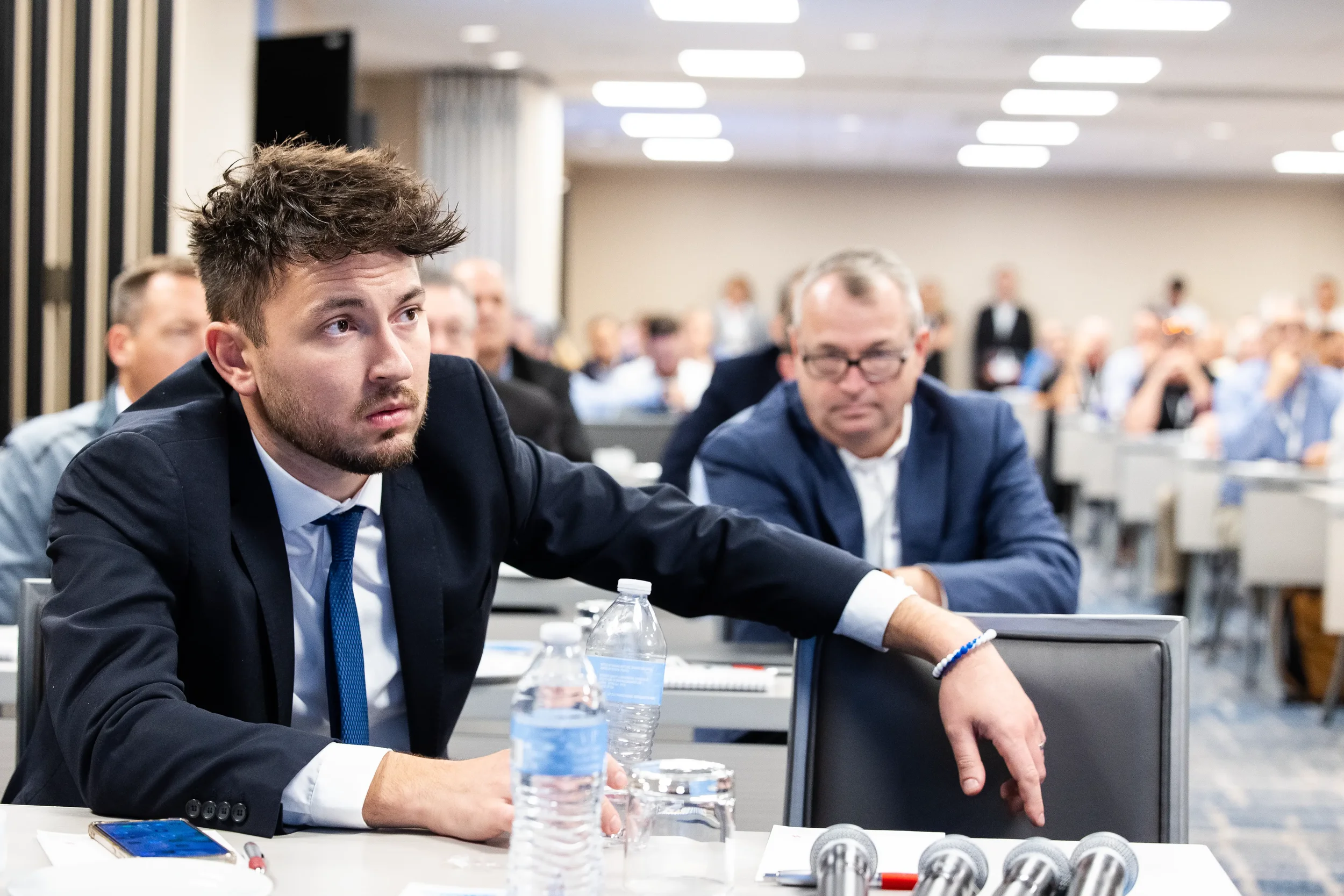 Two attendees in suits lean forward attentively during session in packed ballroom at Chicago industry conference