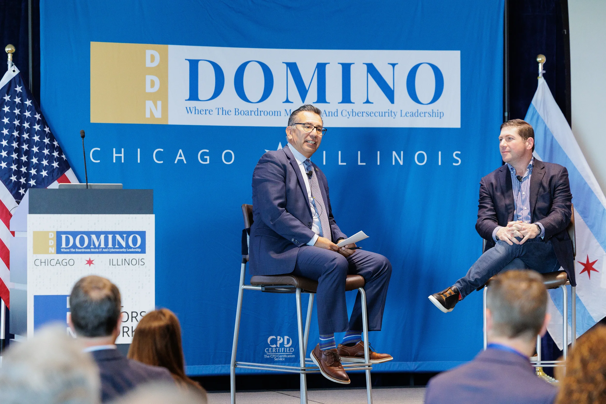 Two speakers seated for fireside chat on branded stage with Chicago flag at Chicago industry conference