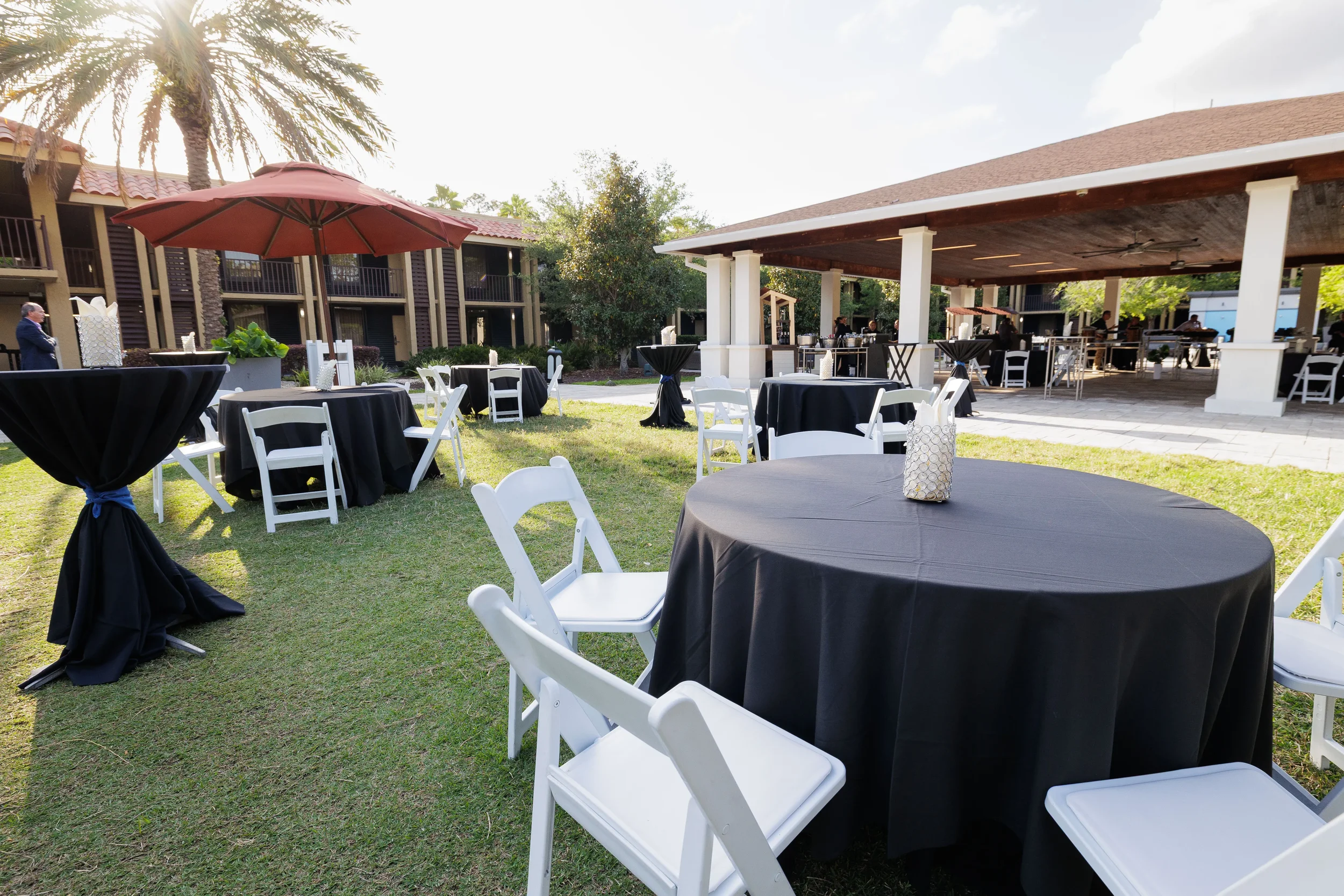 Outdoor reception setup with black-draped round tables and white chairs on hotel grounds at Orlando corporate event
