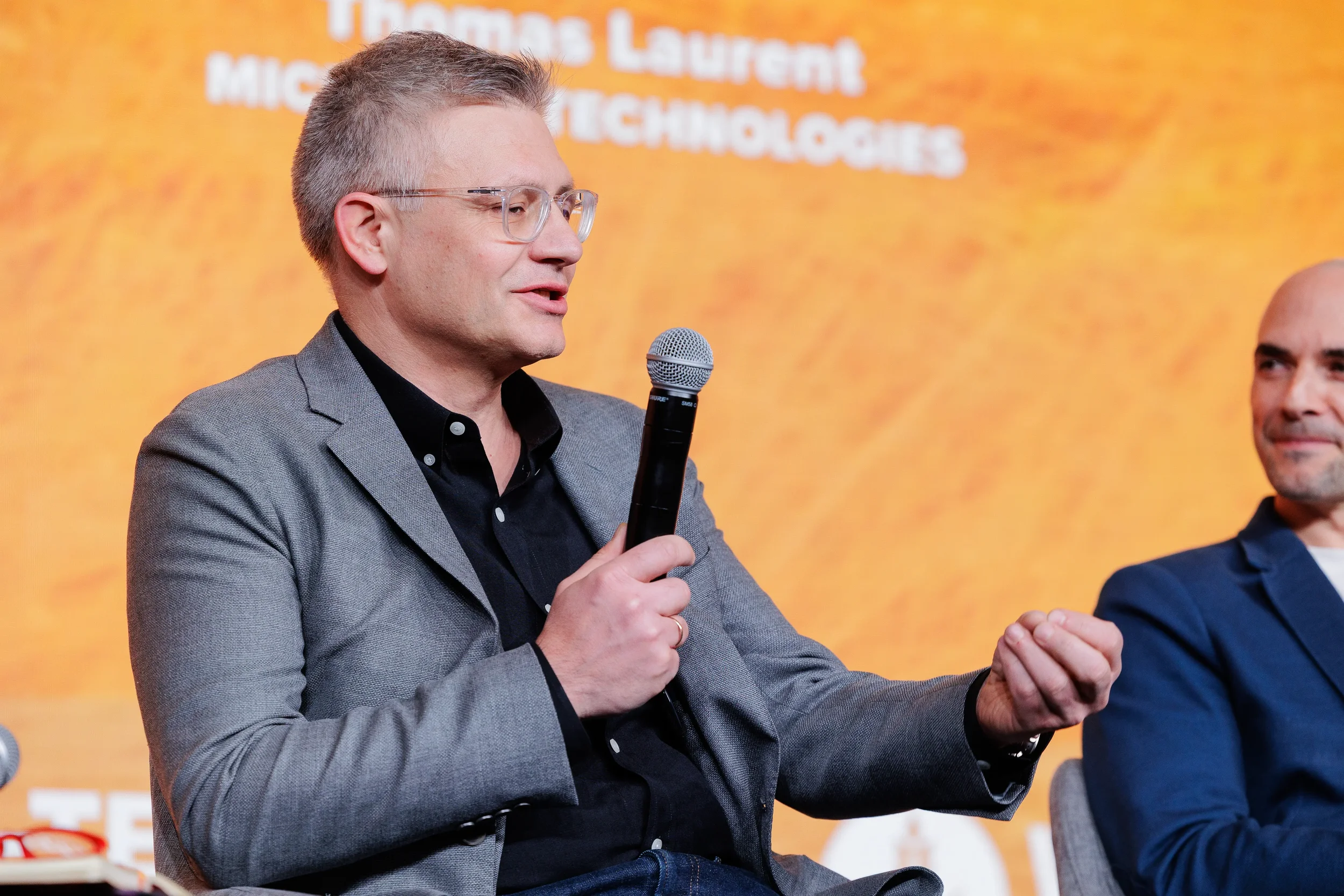 Speaker in gray blazer gestures while presenting with microphone on stage at Chicago industry summit