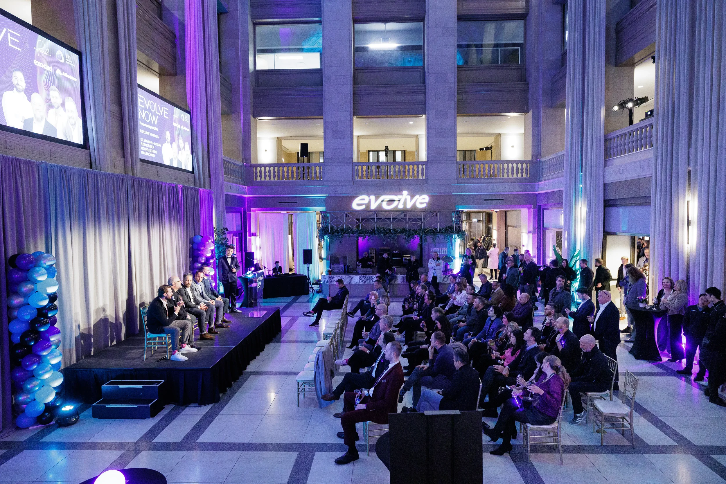 Overhead view of panel on stage and full audience in atrium with illuminated brand sign at Chicago corporate event