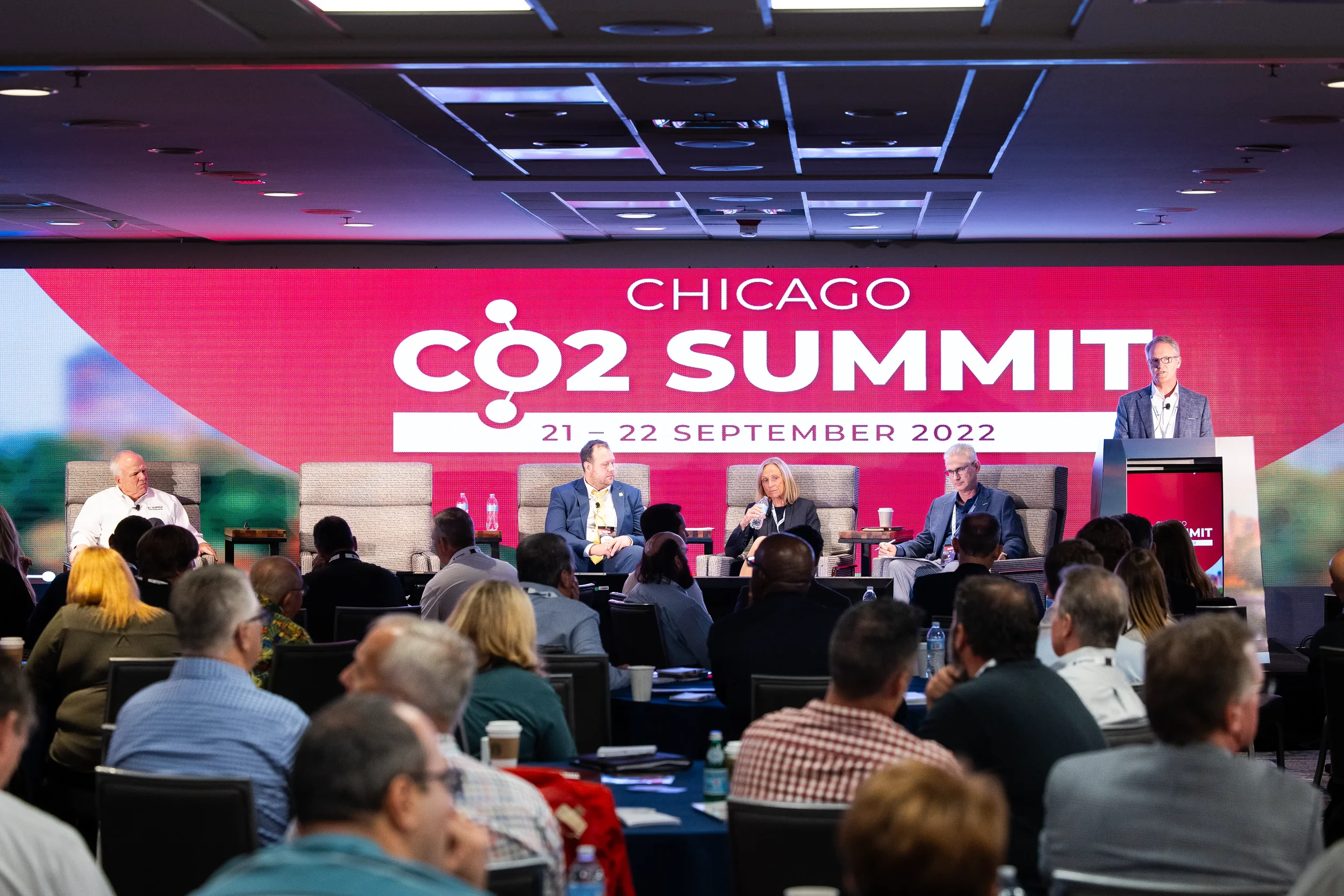 Panelists discuss on stage while moderator speaks from podium in front of audience at Orlando summit