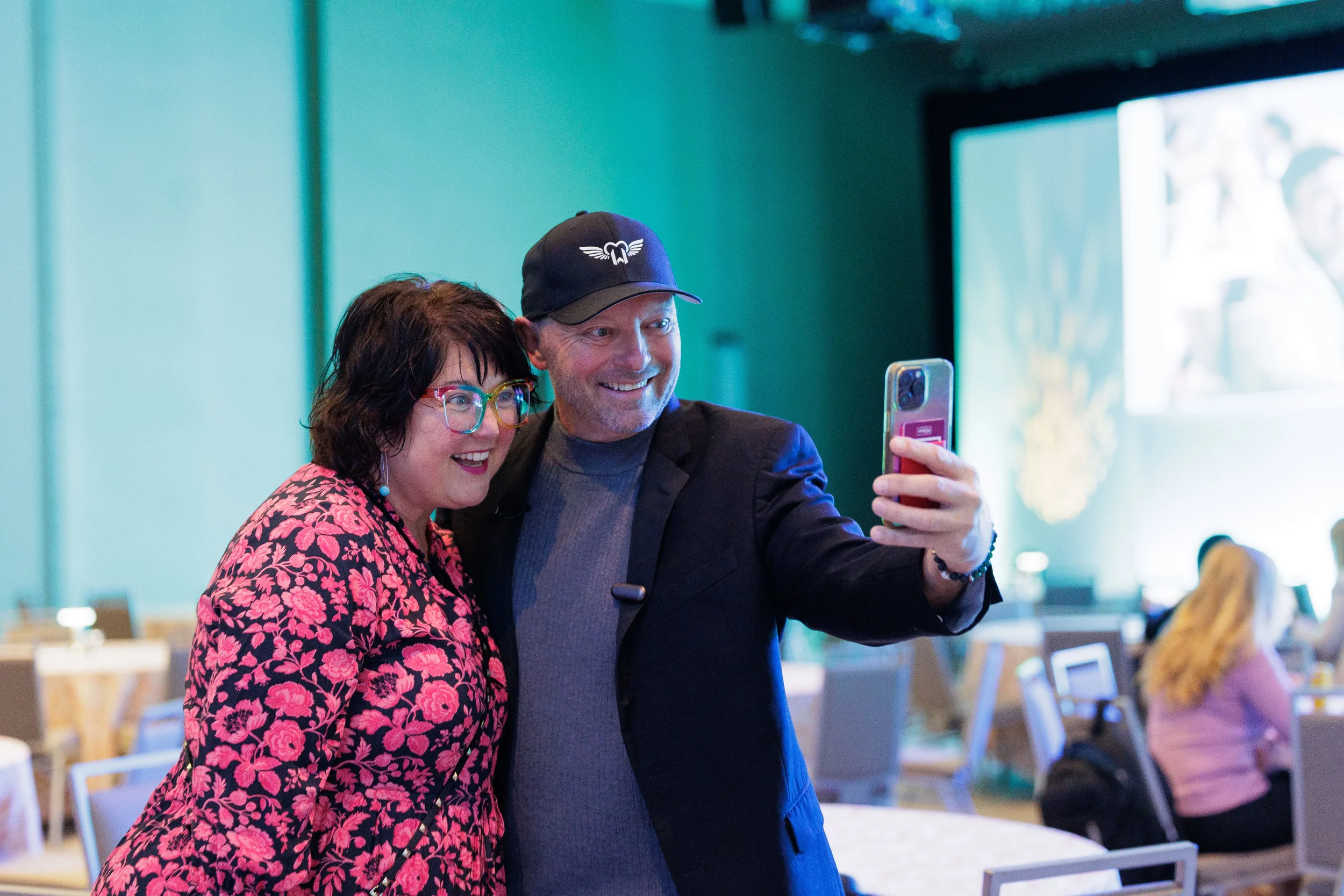 Two smiling attendees take a selfie together in ballroom with green stage lighting at Chicago corporate conference