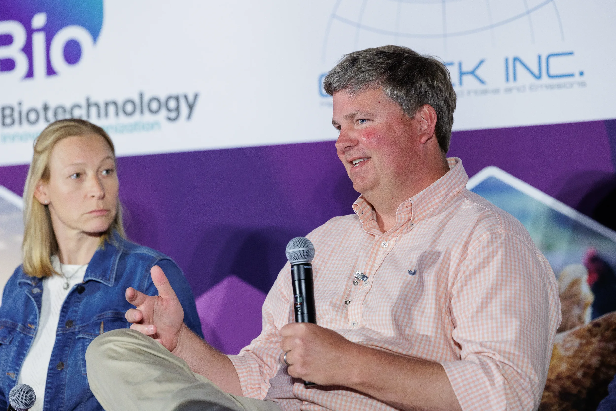 Panelist gestures while speaking into microphone during seated discussion at Orlando corporate conference