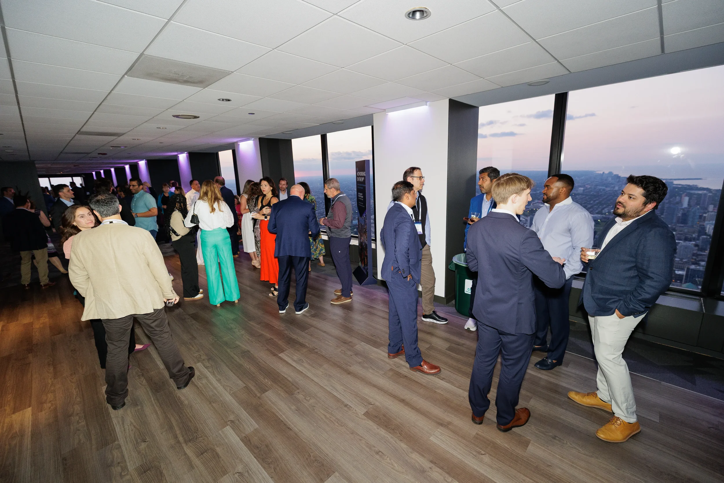 Attendees network with drinks against Chicago skyline view during evening conference reception