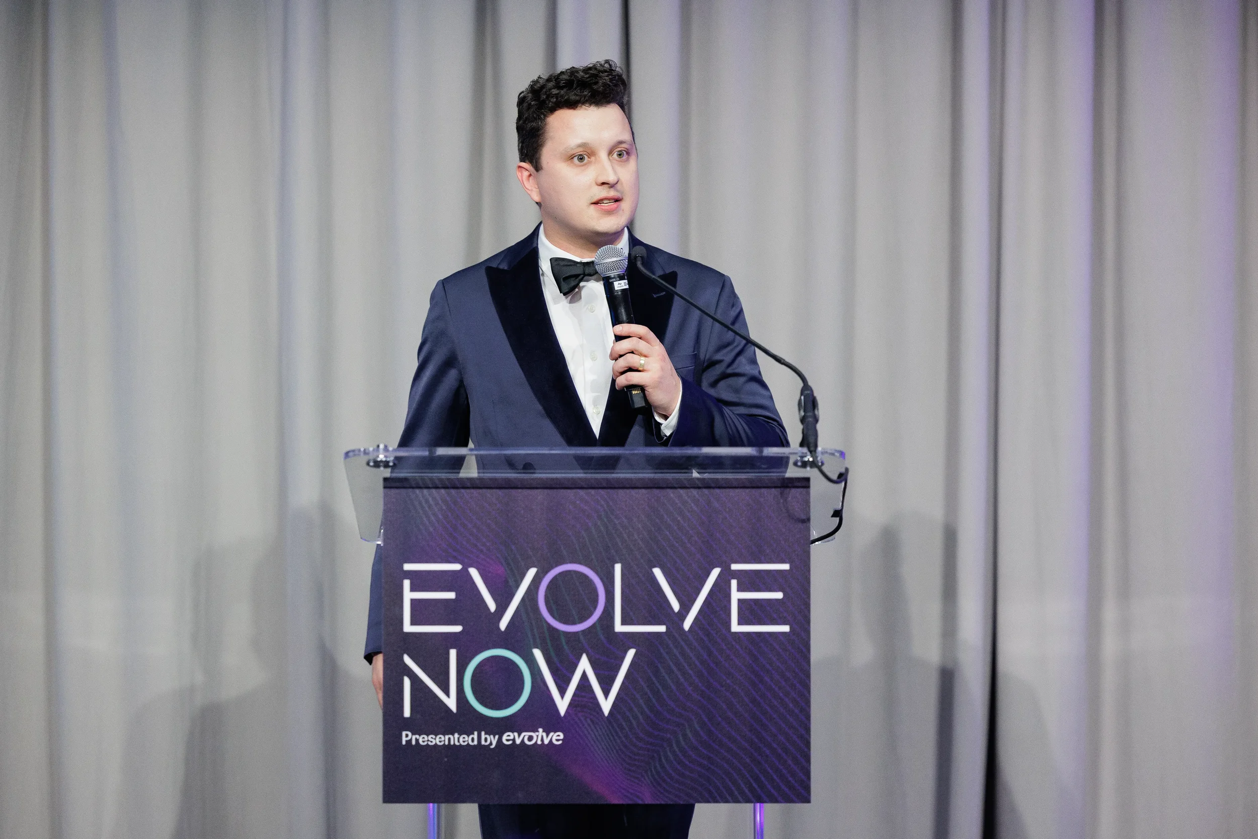 Emcee in navy tuxedo and bow tie speaks at branded podium during Chicago corporate event