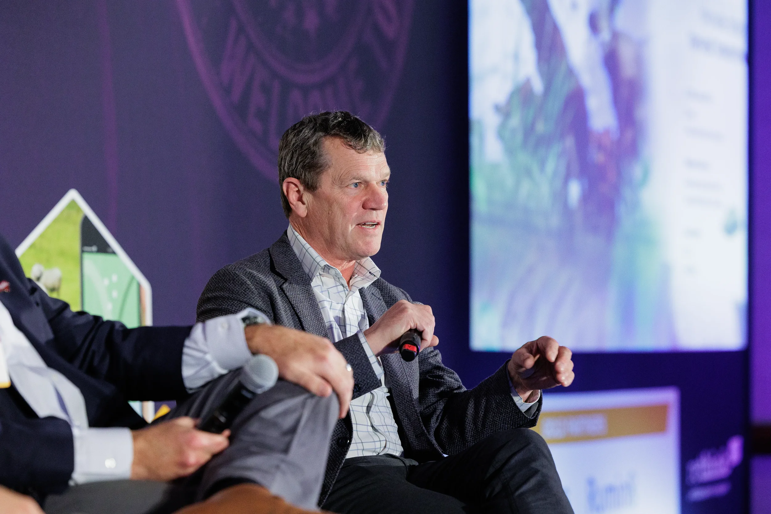 Speaker gestures while holding microphone on branded stage at Orlando industry summit