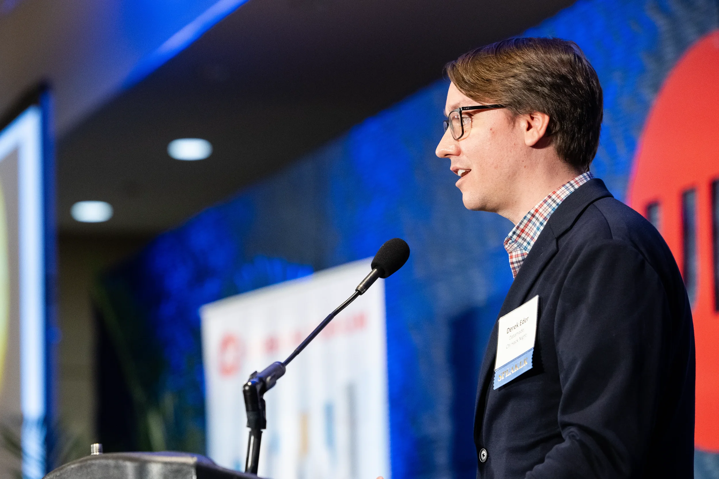 Speaker presents from podium in side profile view on stage at Orlando industry conference