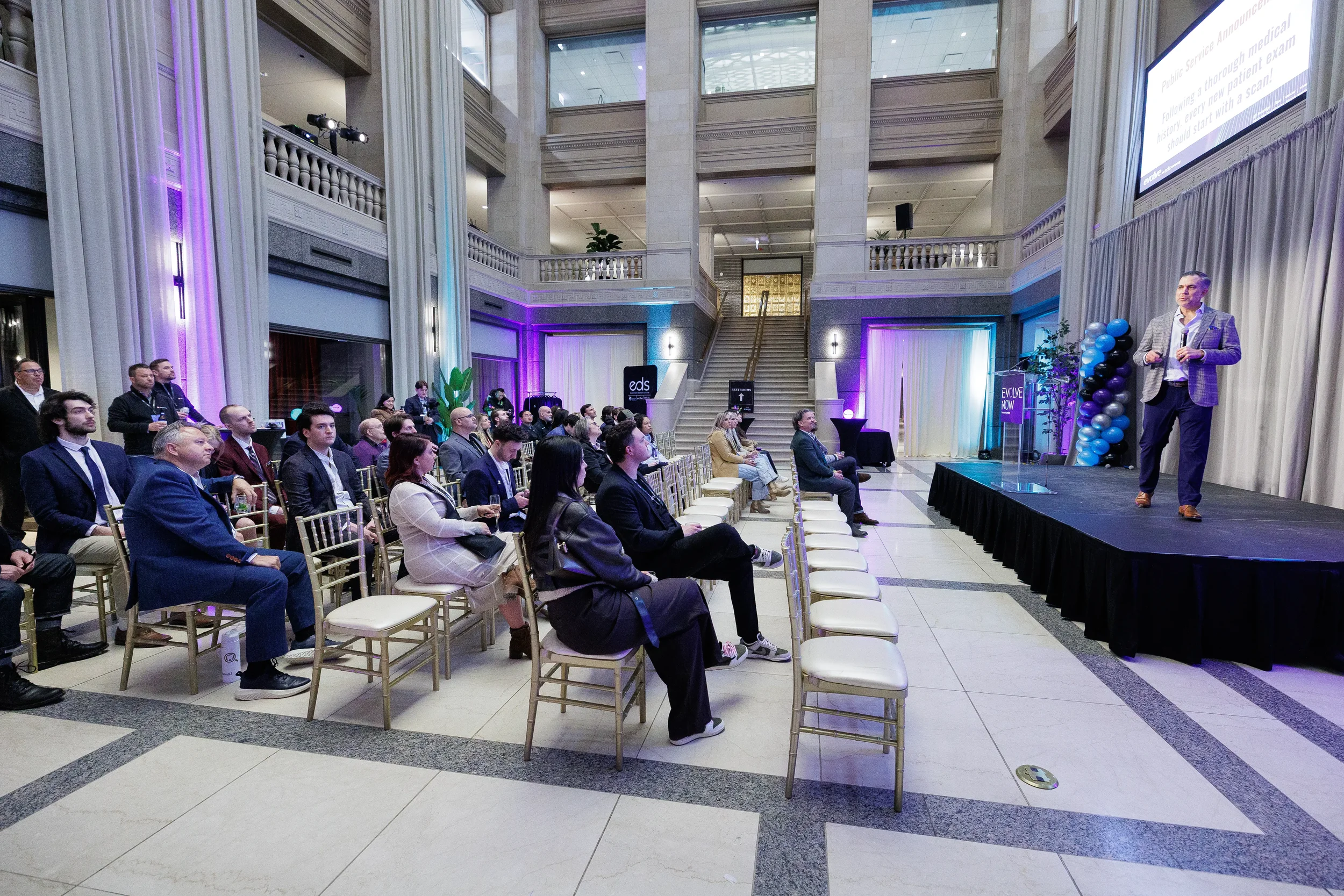 Wide shot of seated audience watching speaker on stage in grand atrium at Chicago corporate event