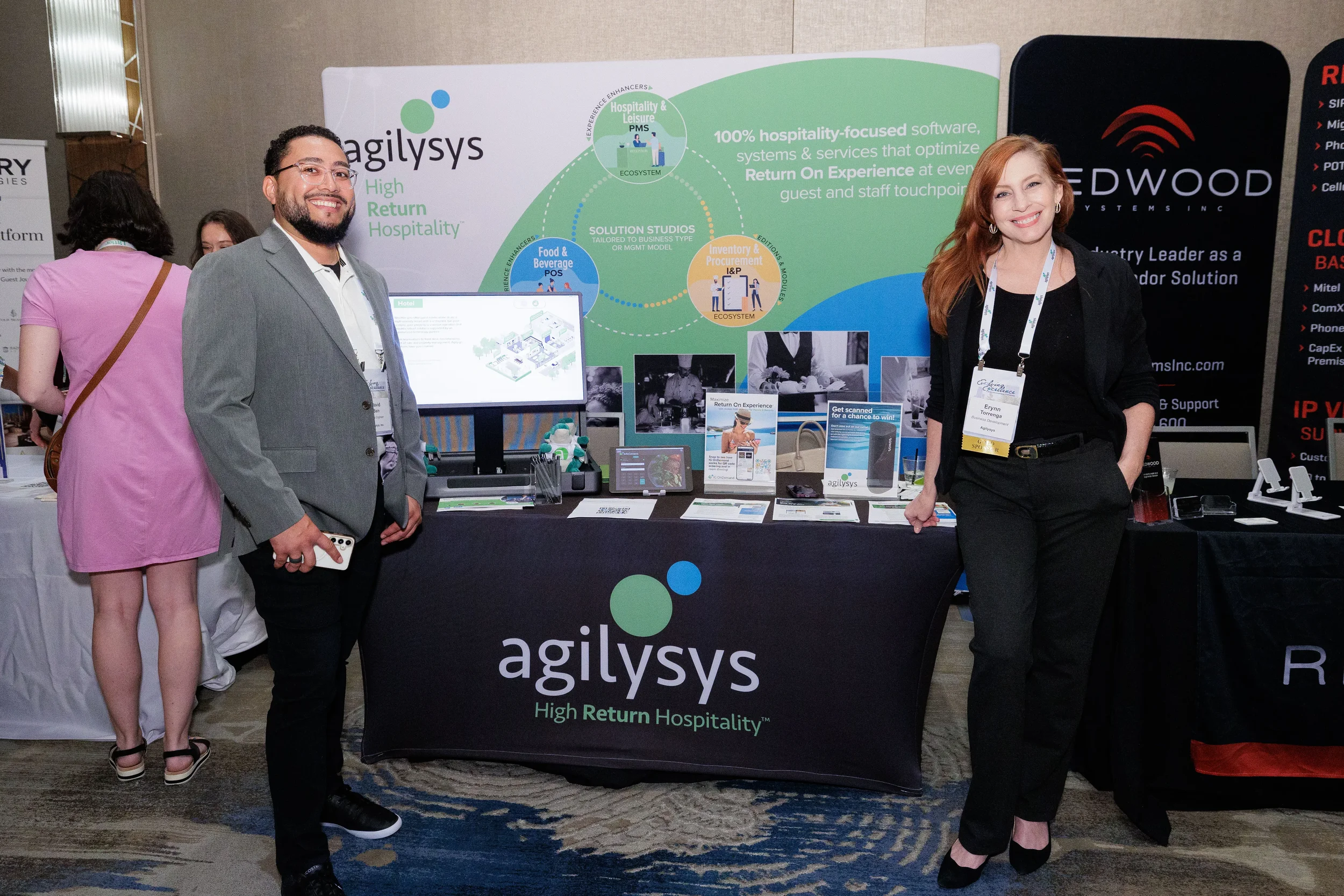 Two booth staff pose beside branded display and monitor at Orlando corporate conference trade show