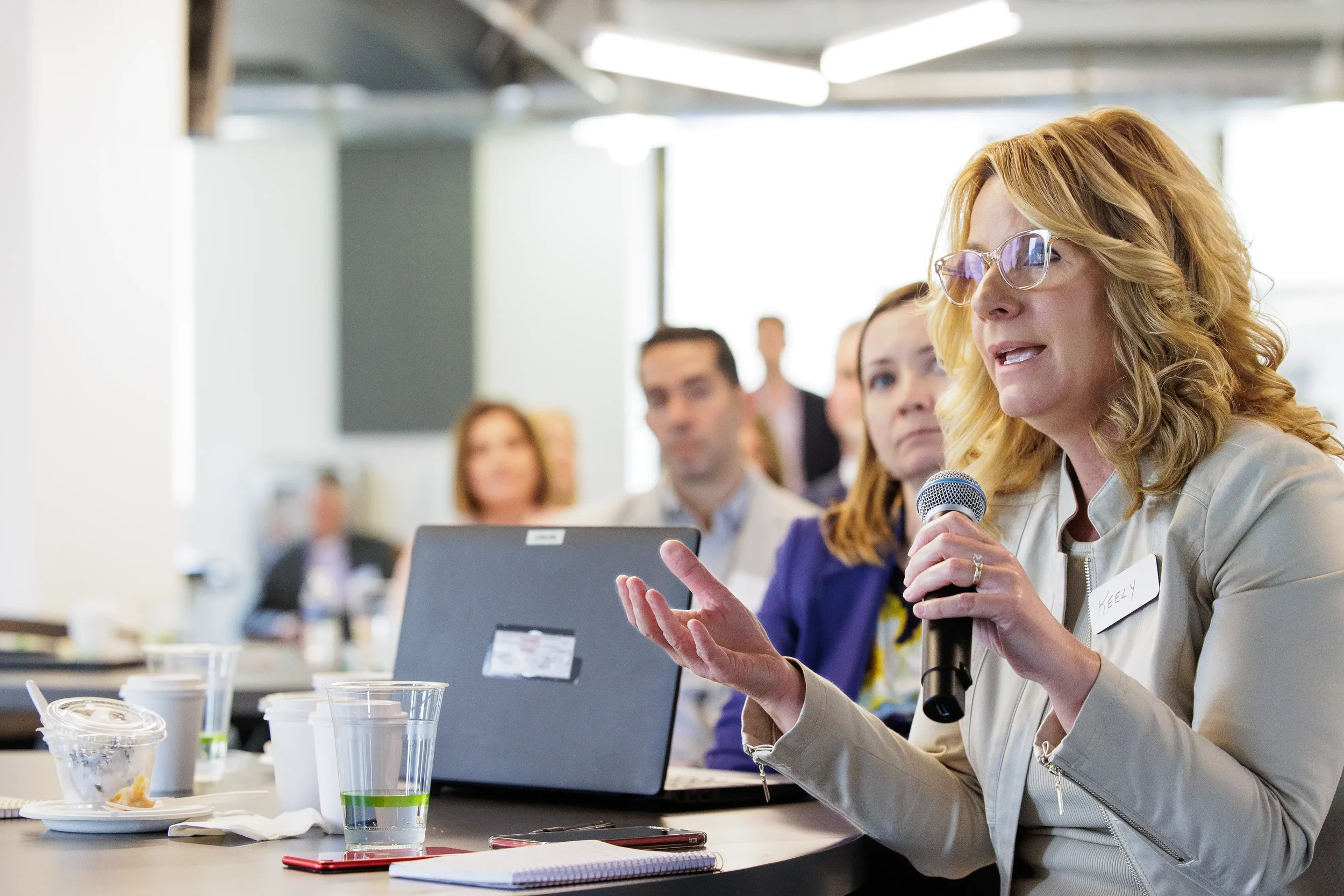 Female attendee speaks into microphone while gesturing at a table during Orlando corporate event session