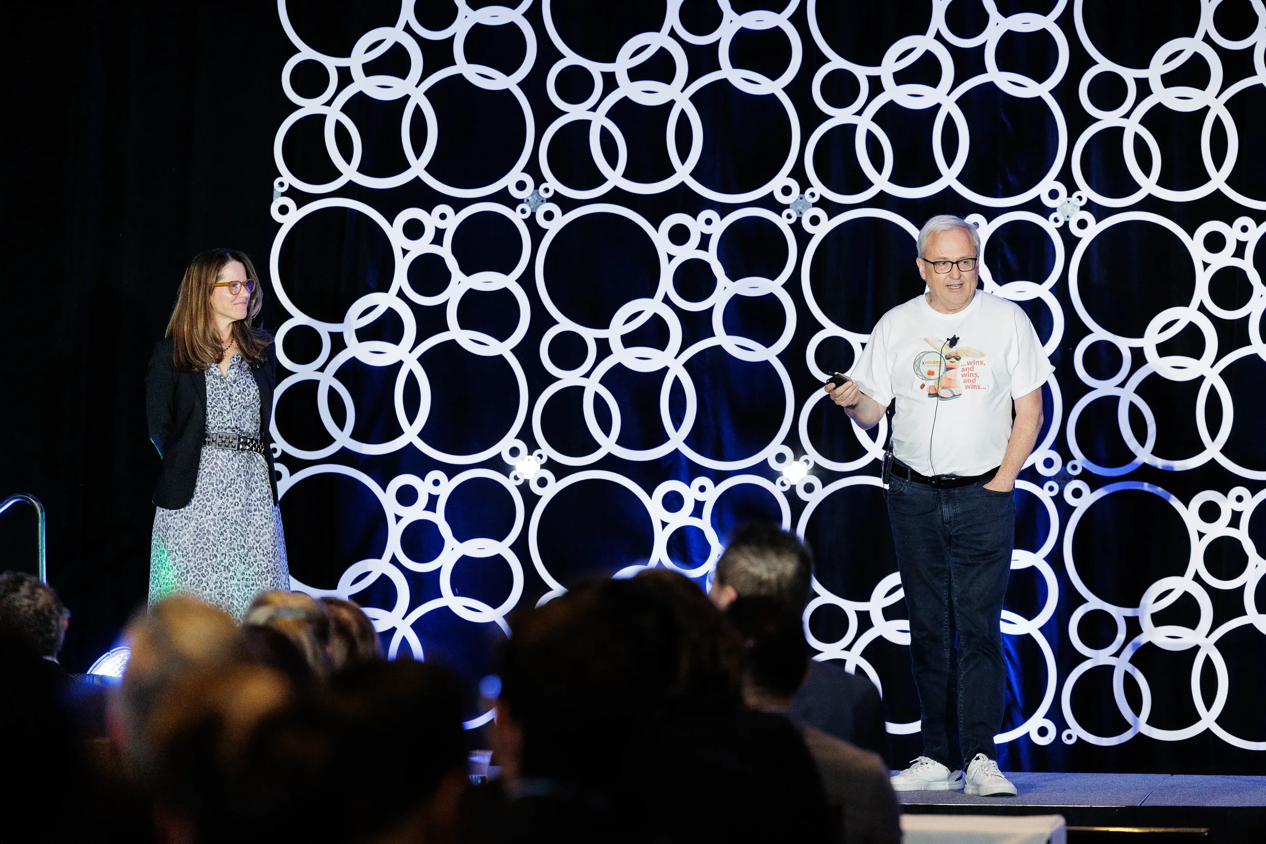 Speaker addresses audience on stage with illuminated circular backdrop at Orlando industry event
