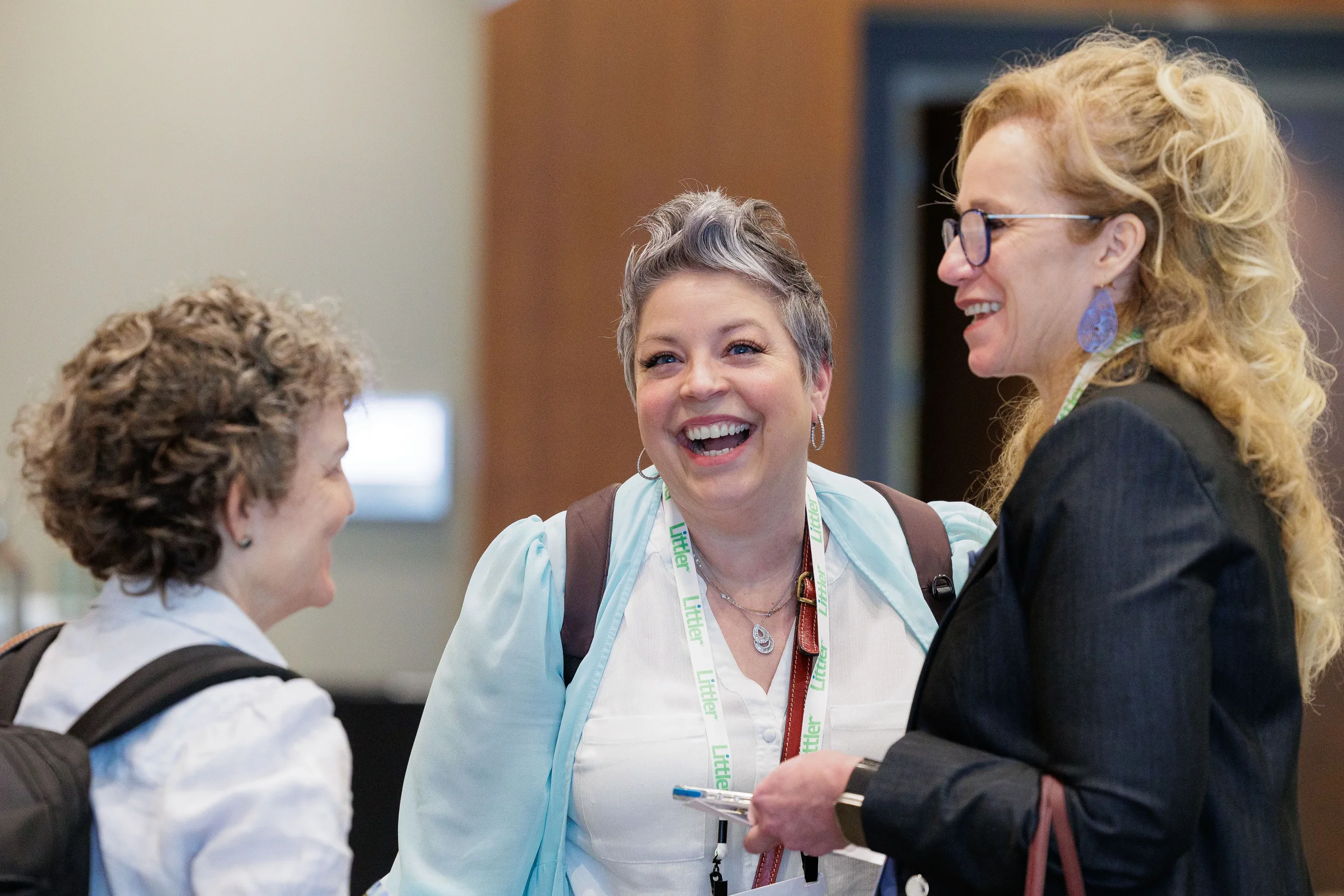 Three female attendees with lanyards laugh together during networking break at Orlando corporate conference