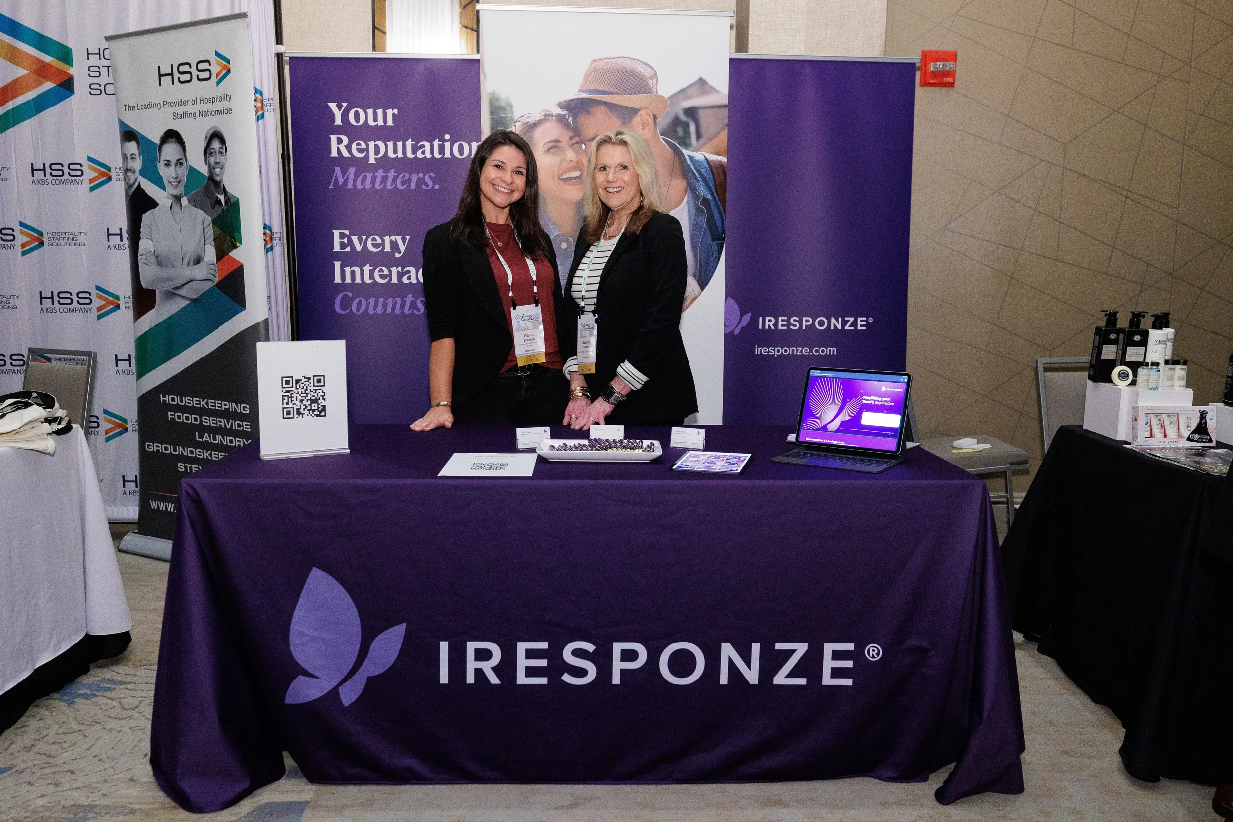 Two booth staff smile behind purple branded table at Orlando corporate conference trade show