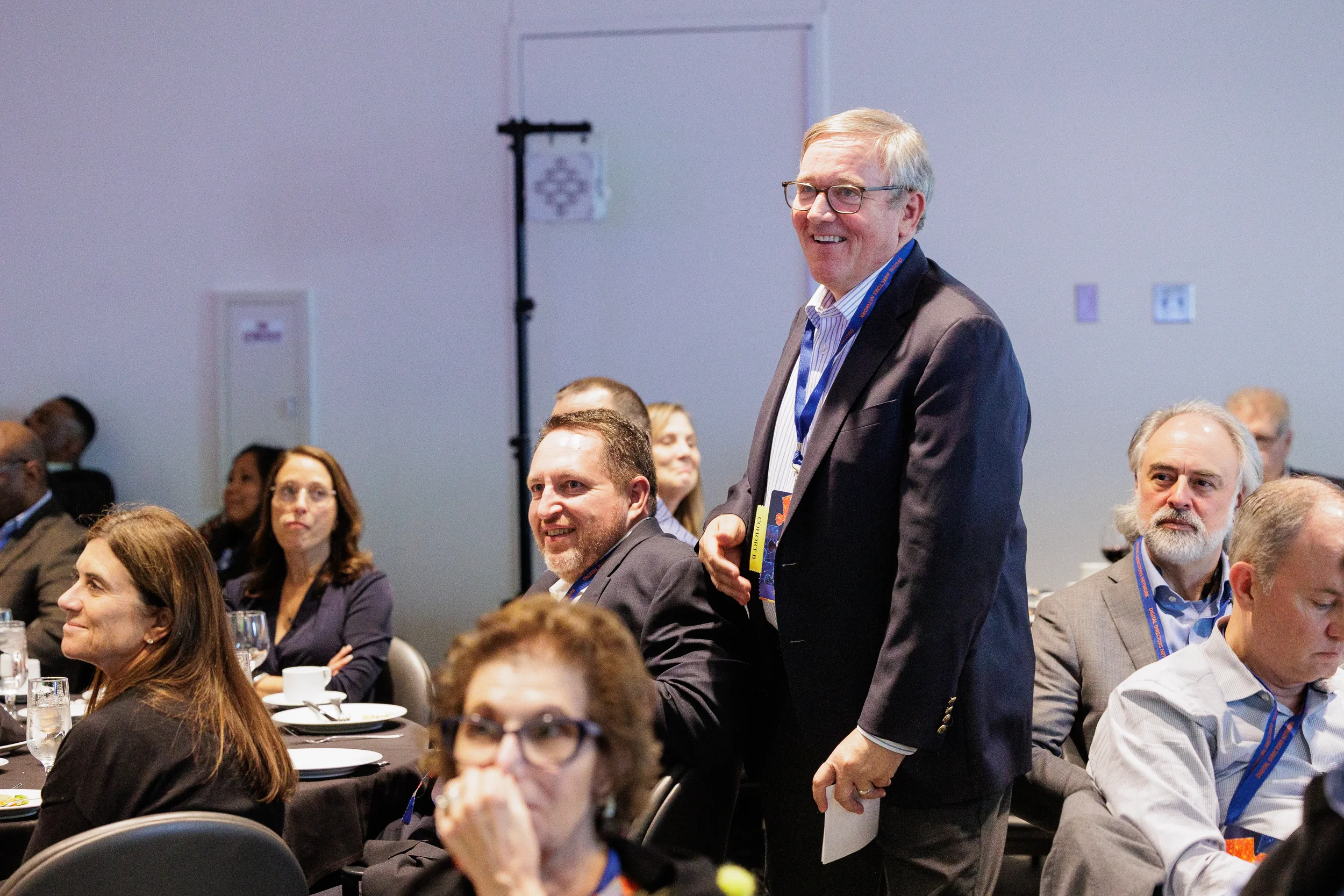 Male attendee with lanyard stands and smiles among seated guests at Orlando corporate conference event