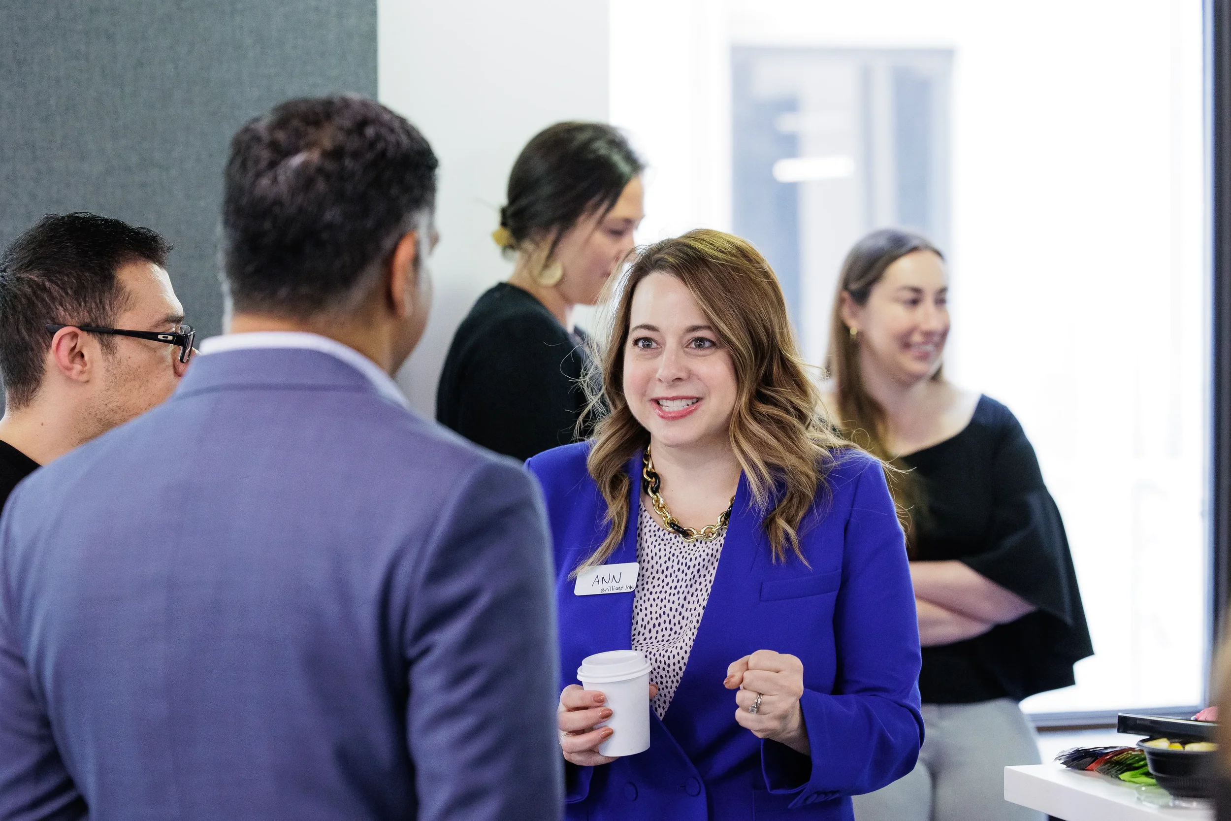Female attendee in blue blazer smiles while networking with coffee in hand at Chicago corporate event