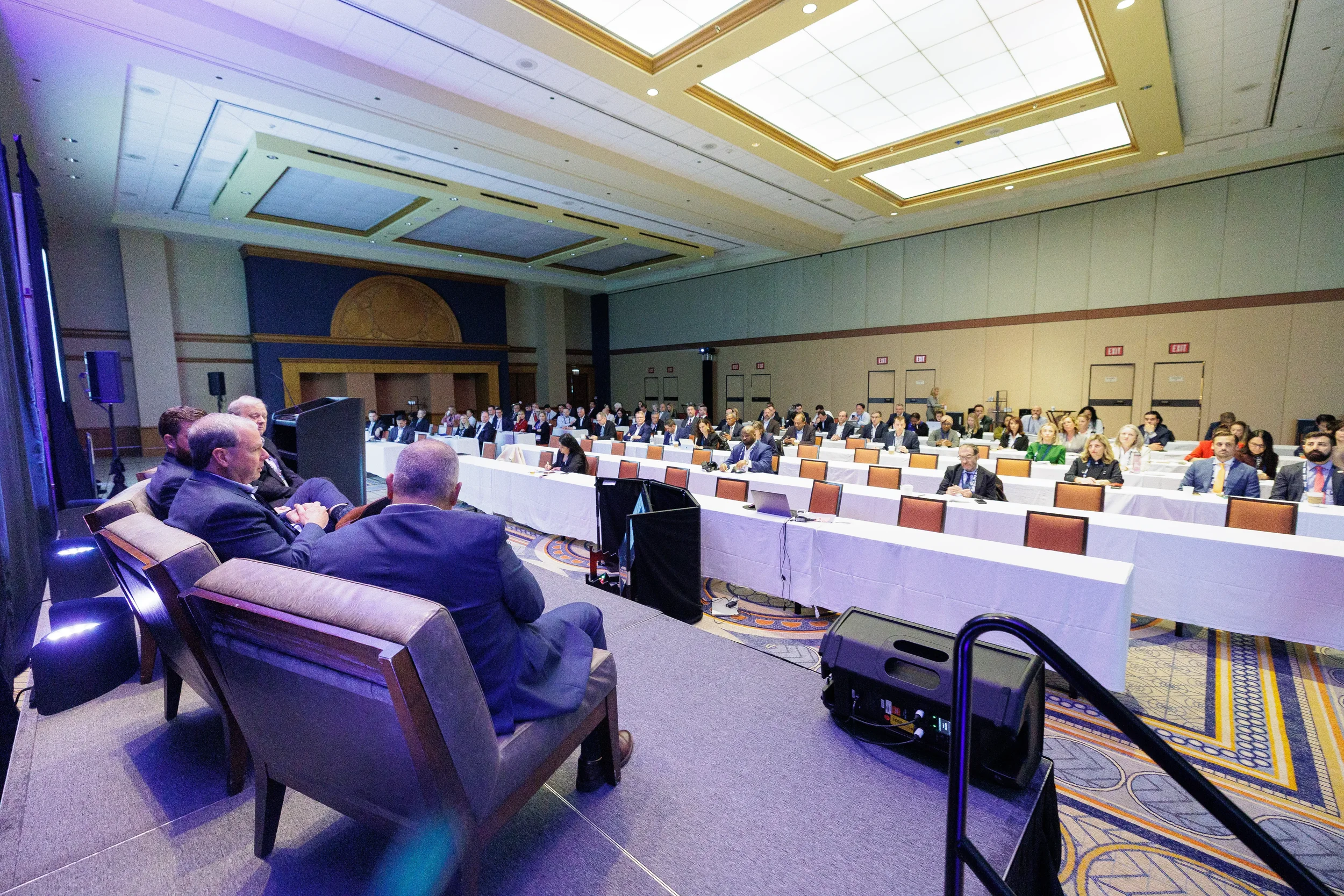 Panelists seated in armchairs face a large audience seated at banquet tables in a brightly lit conference hall in Chicago.