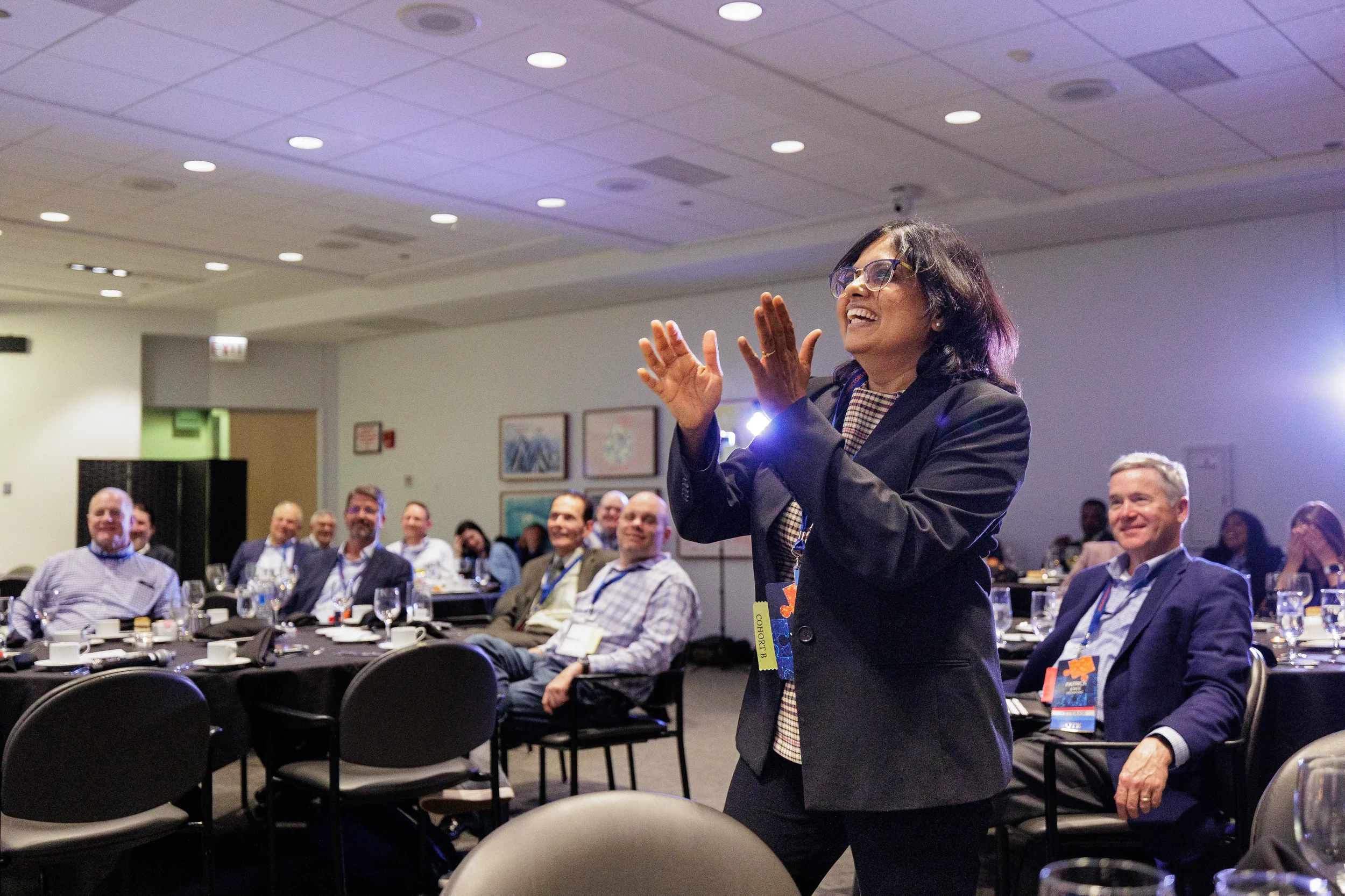 Female speaker with lanyard gestures enthusiastically before laughing audience at Orlando corporate conference