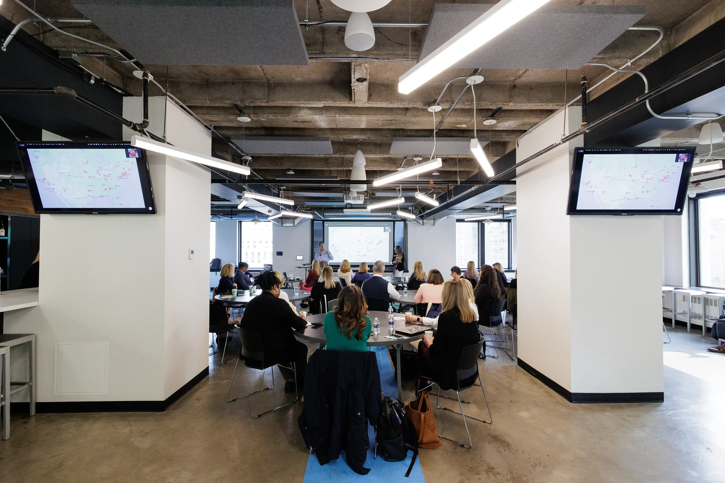 Wide view of full conference room with dual overhead screens and presenter at front at Orlando conference