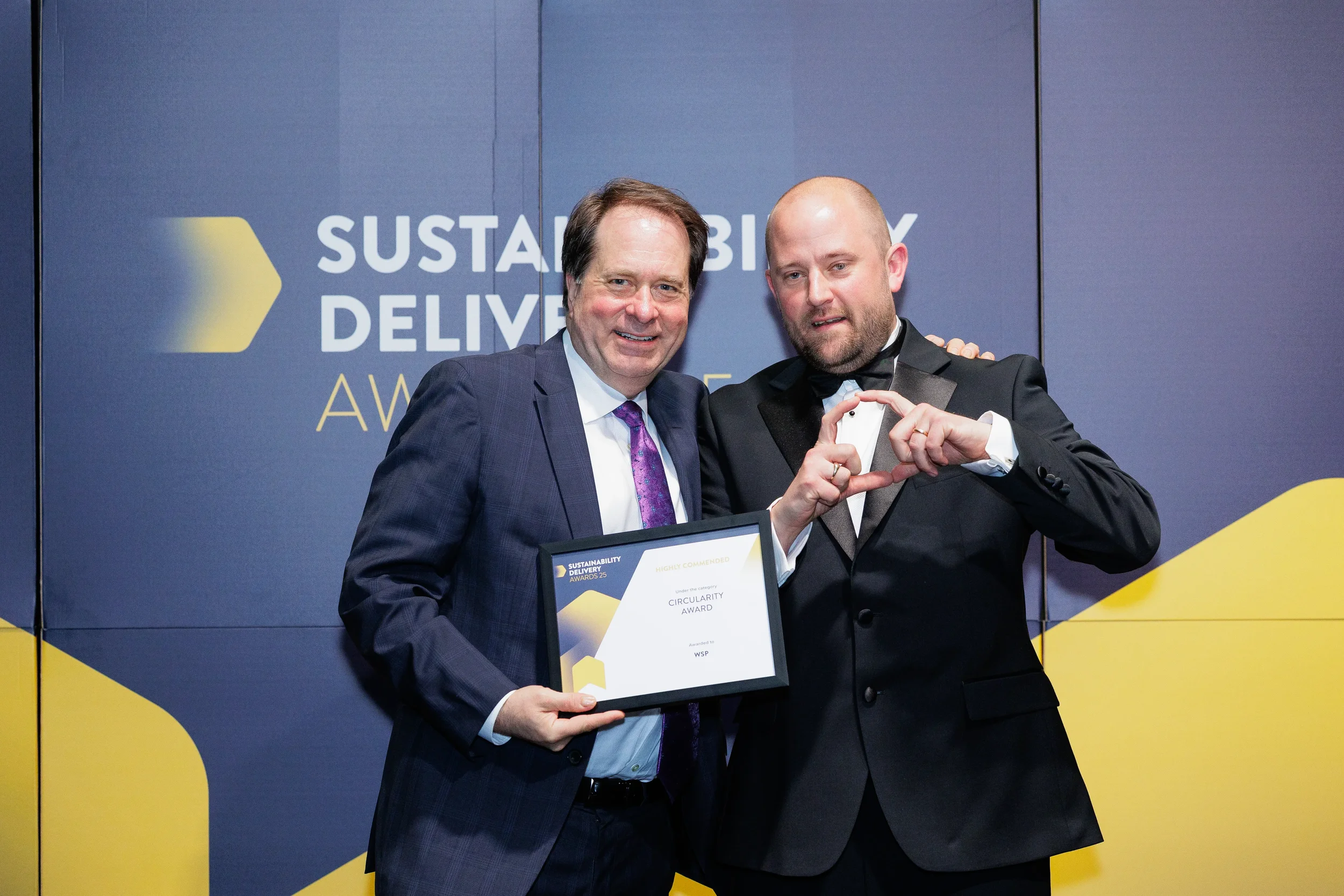Two award recipients pose making heart hands with certificate at Chicago corporate awards ceremony