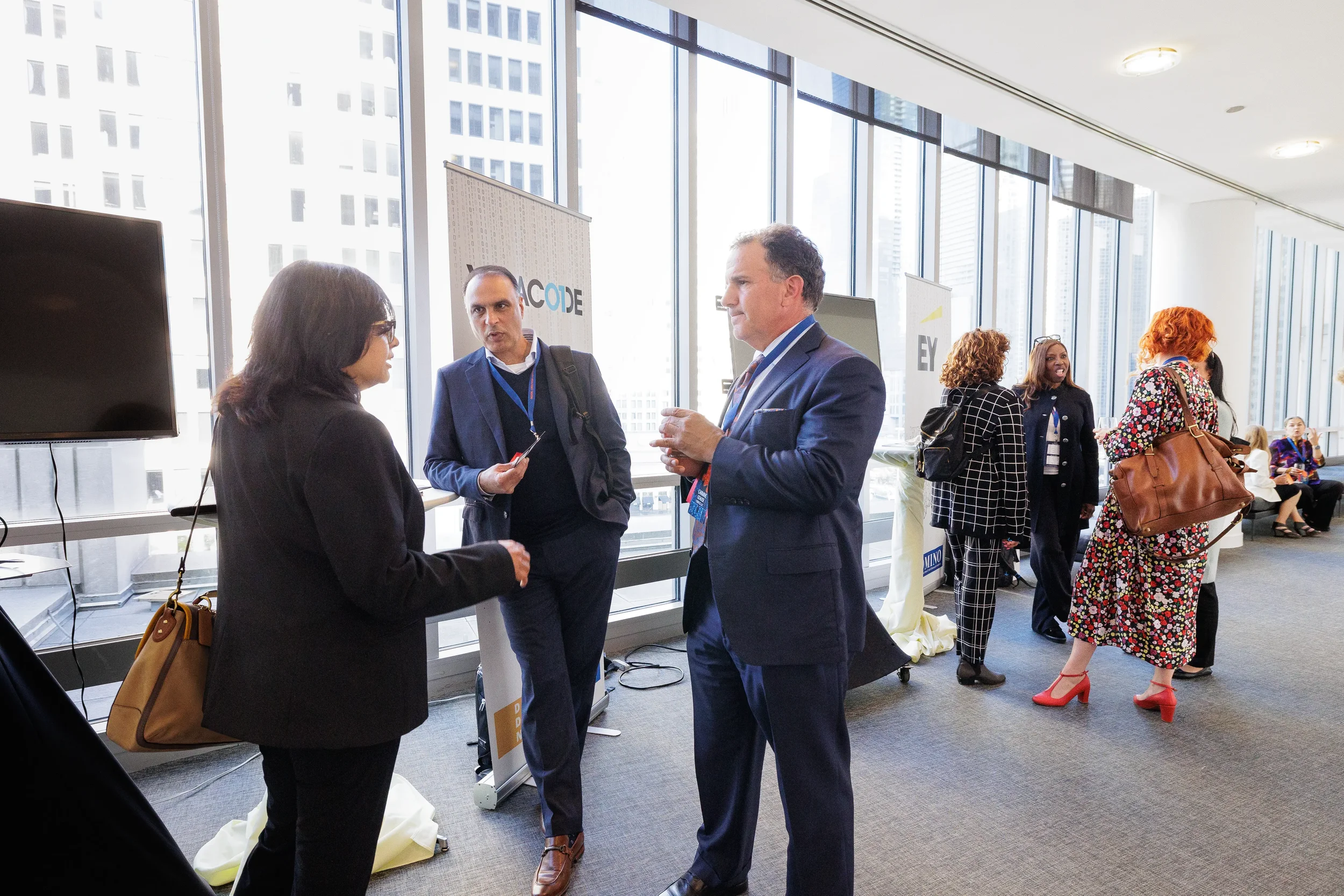 Attendees network near sponsor banners with floor-to-ceiling city views at Orlando corporate conference