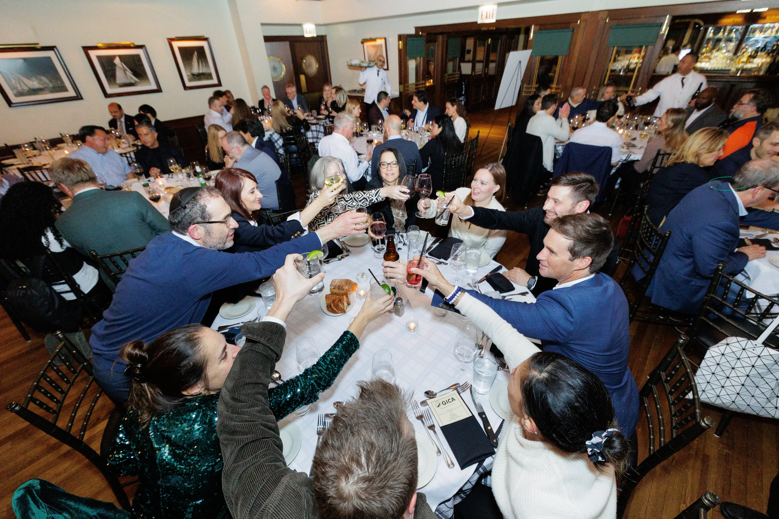 A group in business casual attire raise their drinks in a toast around a circular dinner table in a Chicago restaurant.