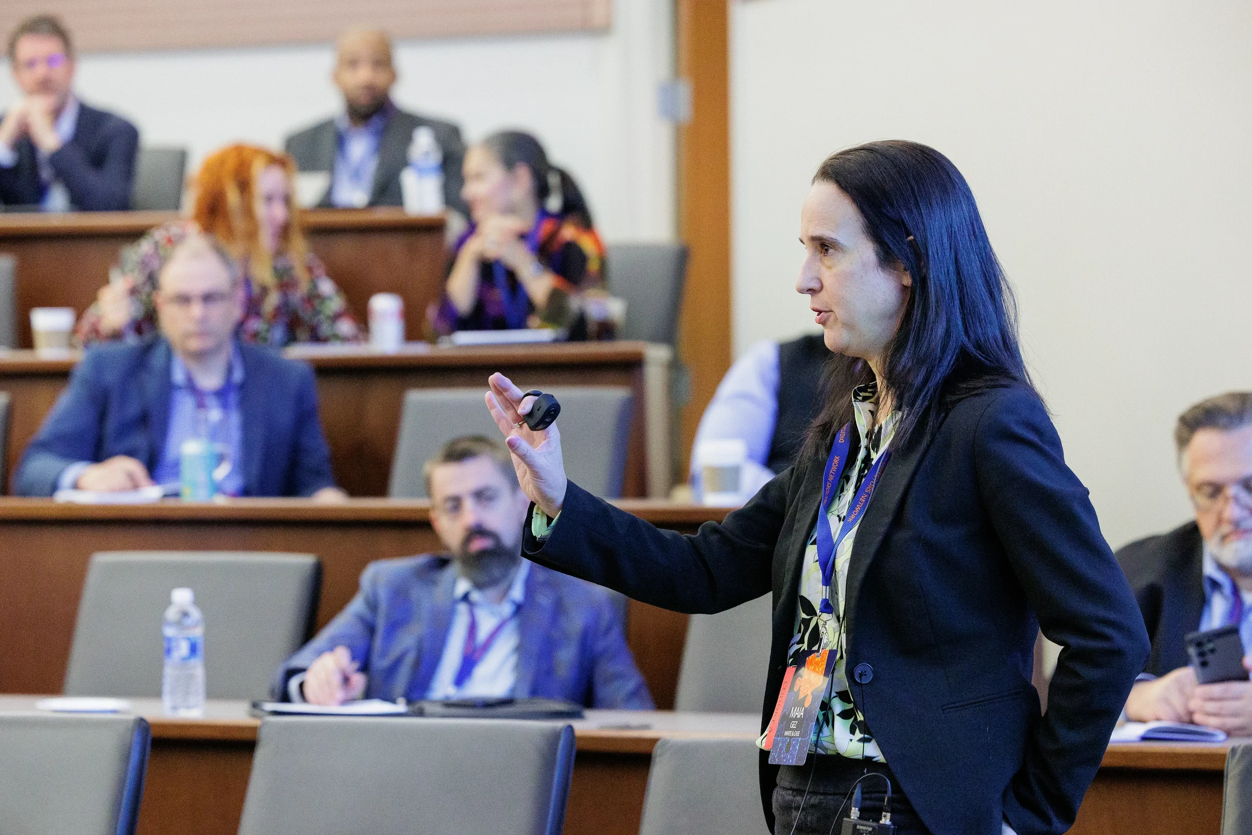 Female speaker with clicker and lanyard presents to tiered audience at Orlando industry conference