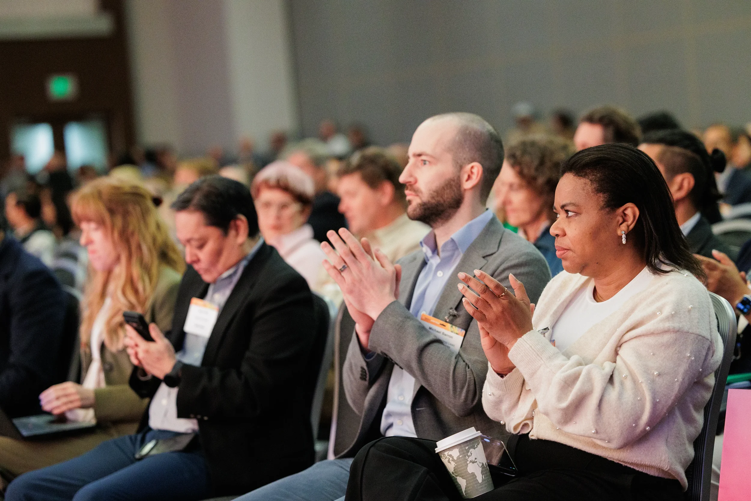 Attendees with name badges applaud during session seated in rows at Orlando corporate industry conference