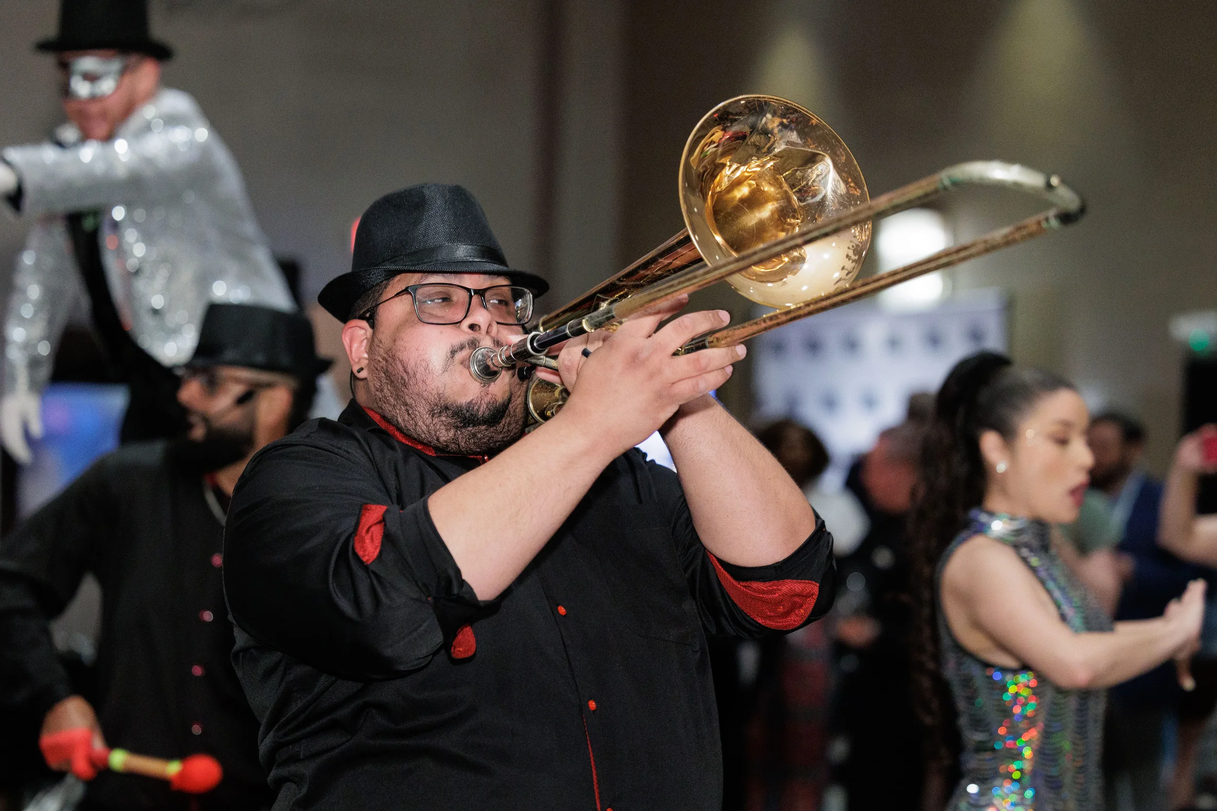 Live band trombone player performs in black hat alongside sequin dancer at Chicago corporate conference expo
