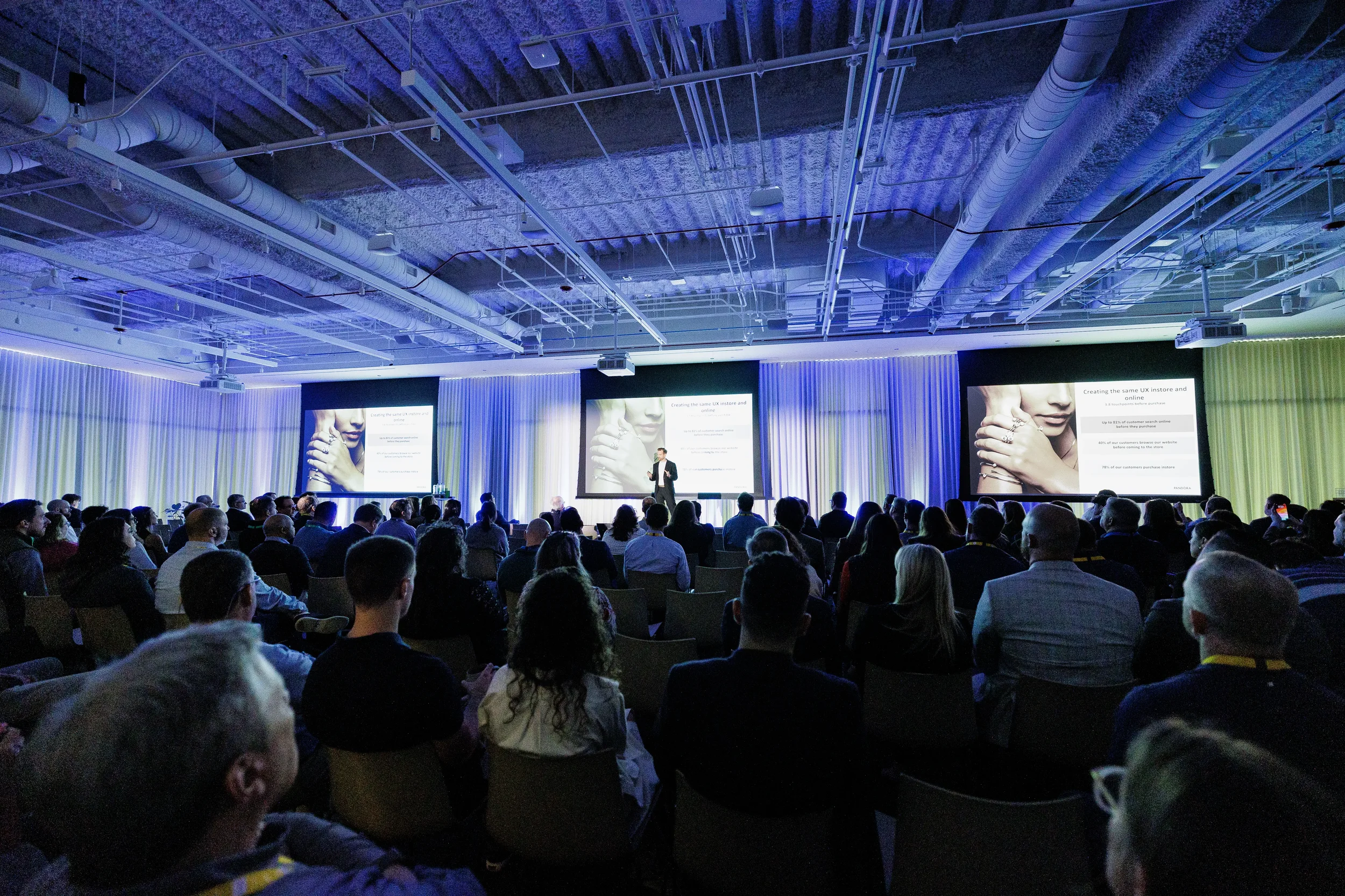 Packed audience watches speaker present before three screens at Orlando corporate conference session