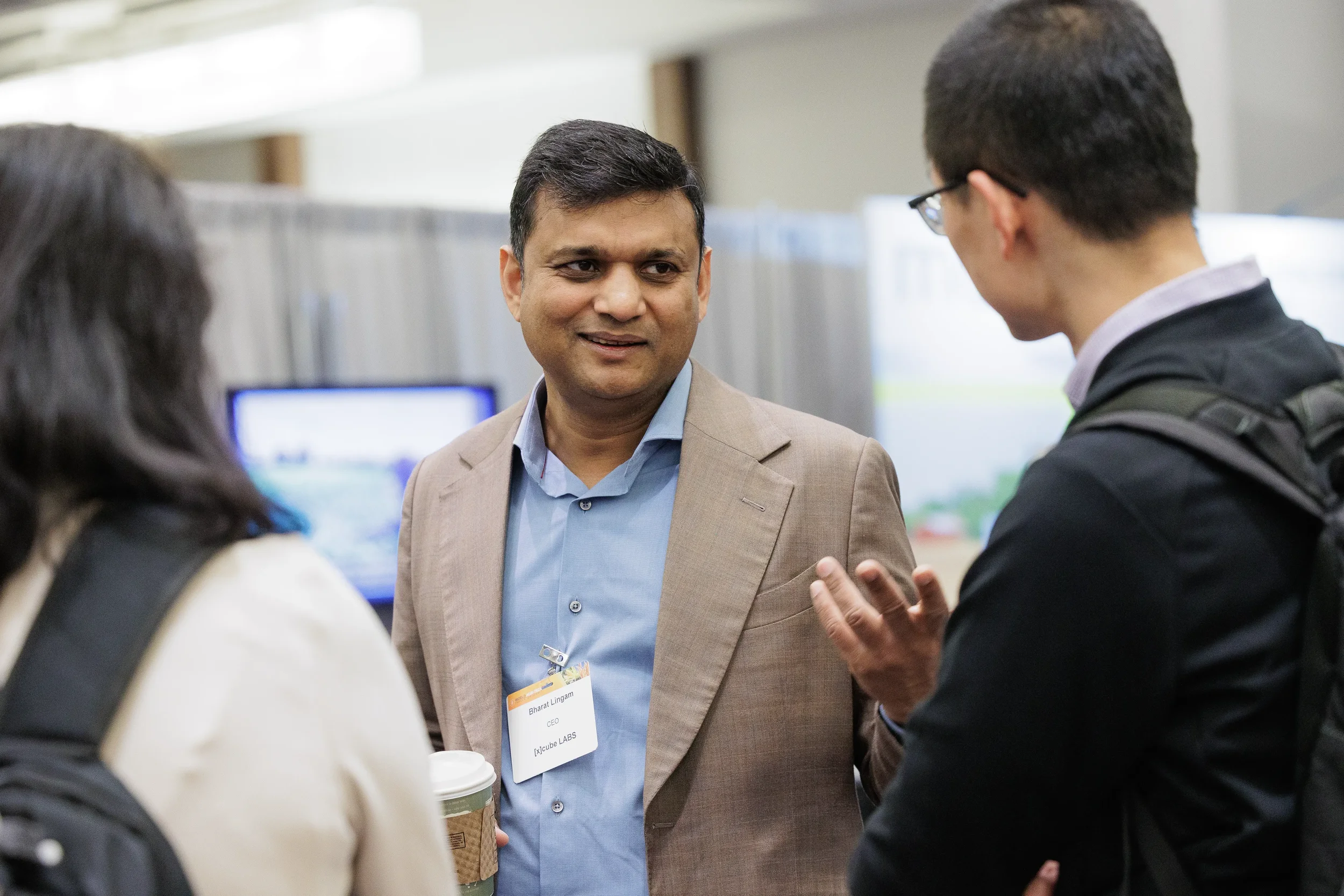 Badged attendee with coffee converses with two others during networking at Chicago corporate conference