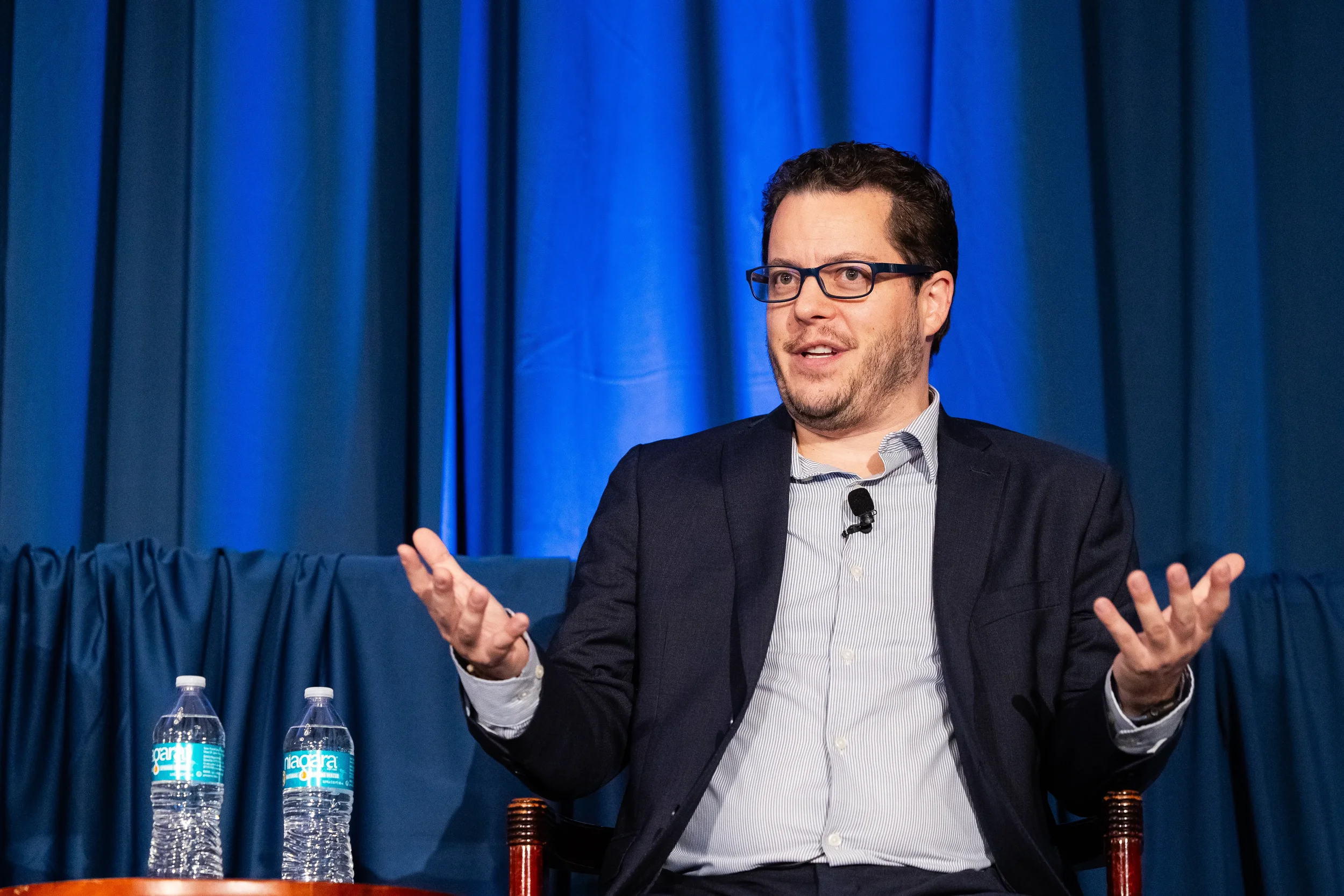 Conference panelist in navy blazer speaks passionately on stage at Orlando corporate event