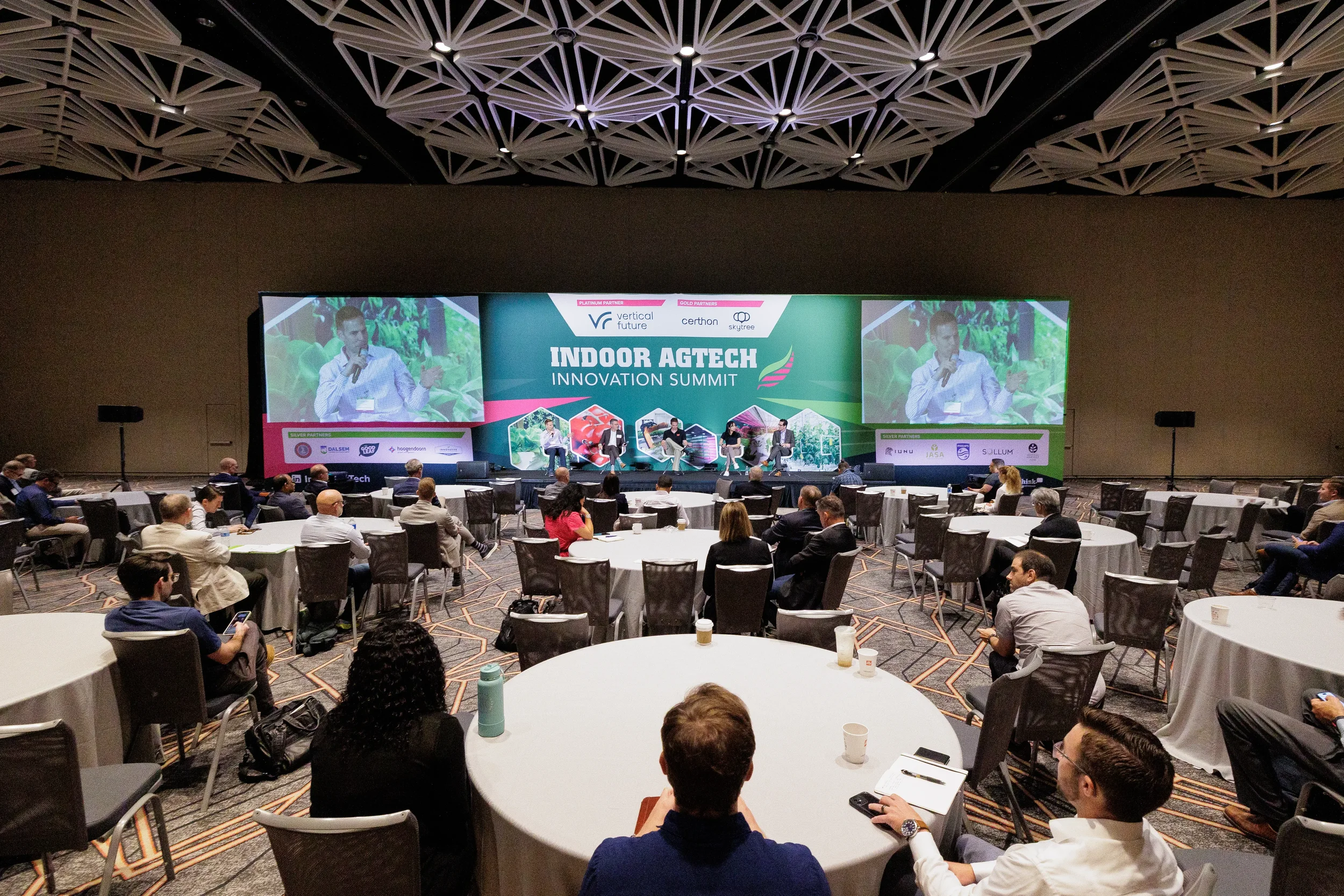 Attendees seated at round tables watch panel discussion on stage in ballroom at Orlando industry conference