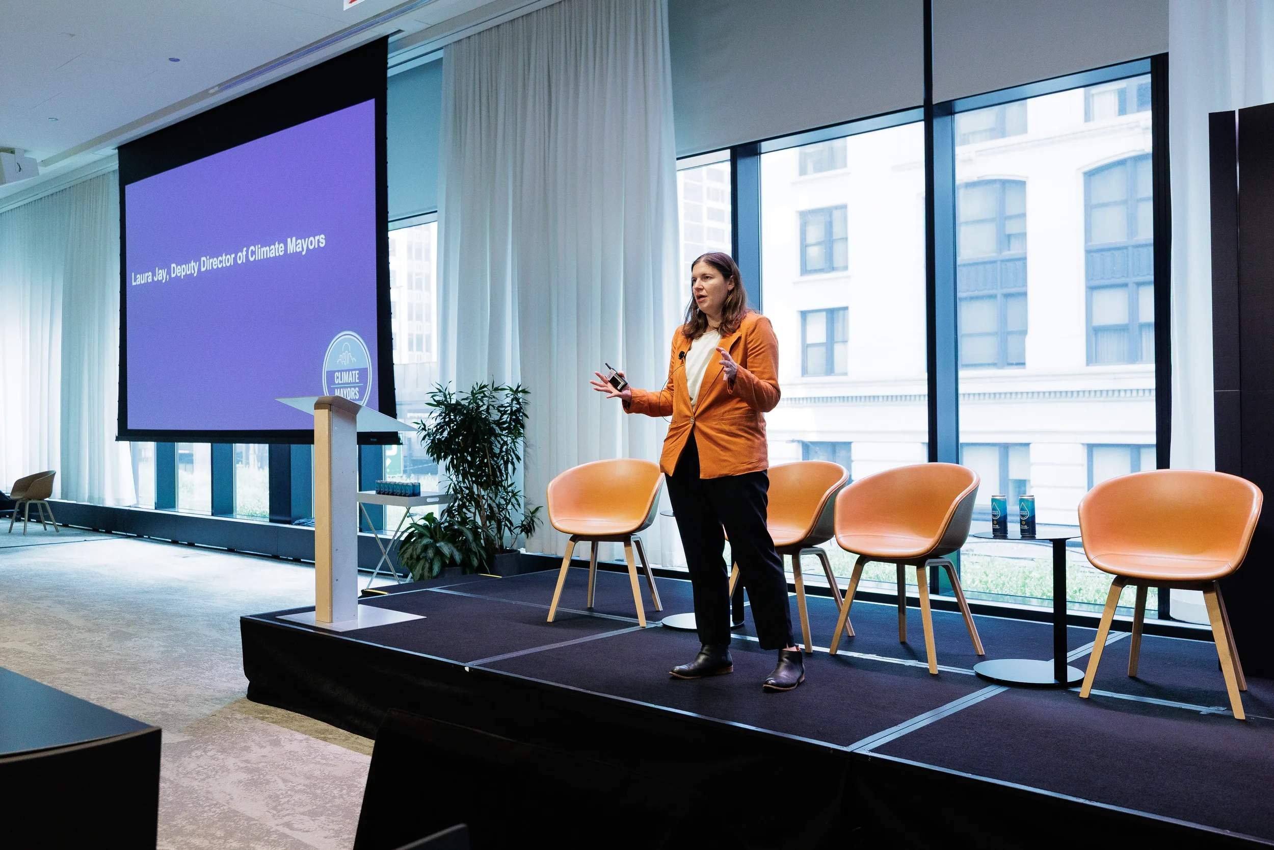 Speaker gestures on stage in front of presentation screen at Orlando industry summit