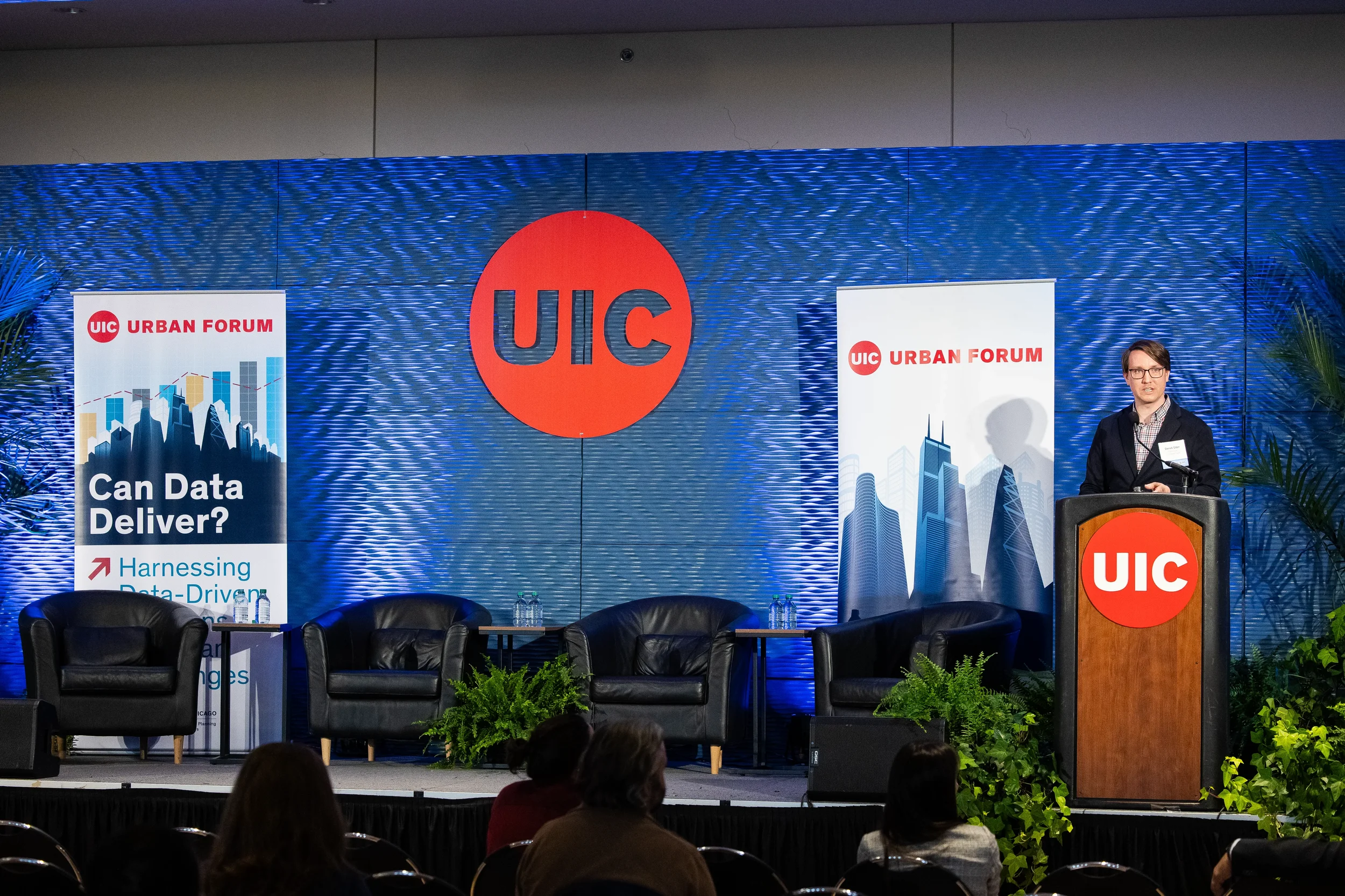 Speaker addresses audience from podium beside empty panel chairs at Chicago corporate conference