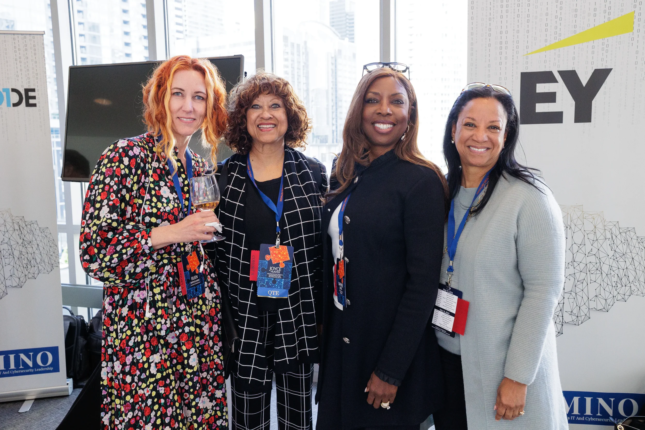 Four female attendees with lanyards smile together near sponsor banners at Orlando industry conference reception