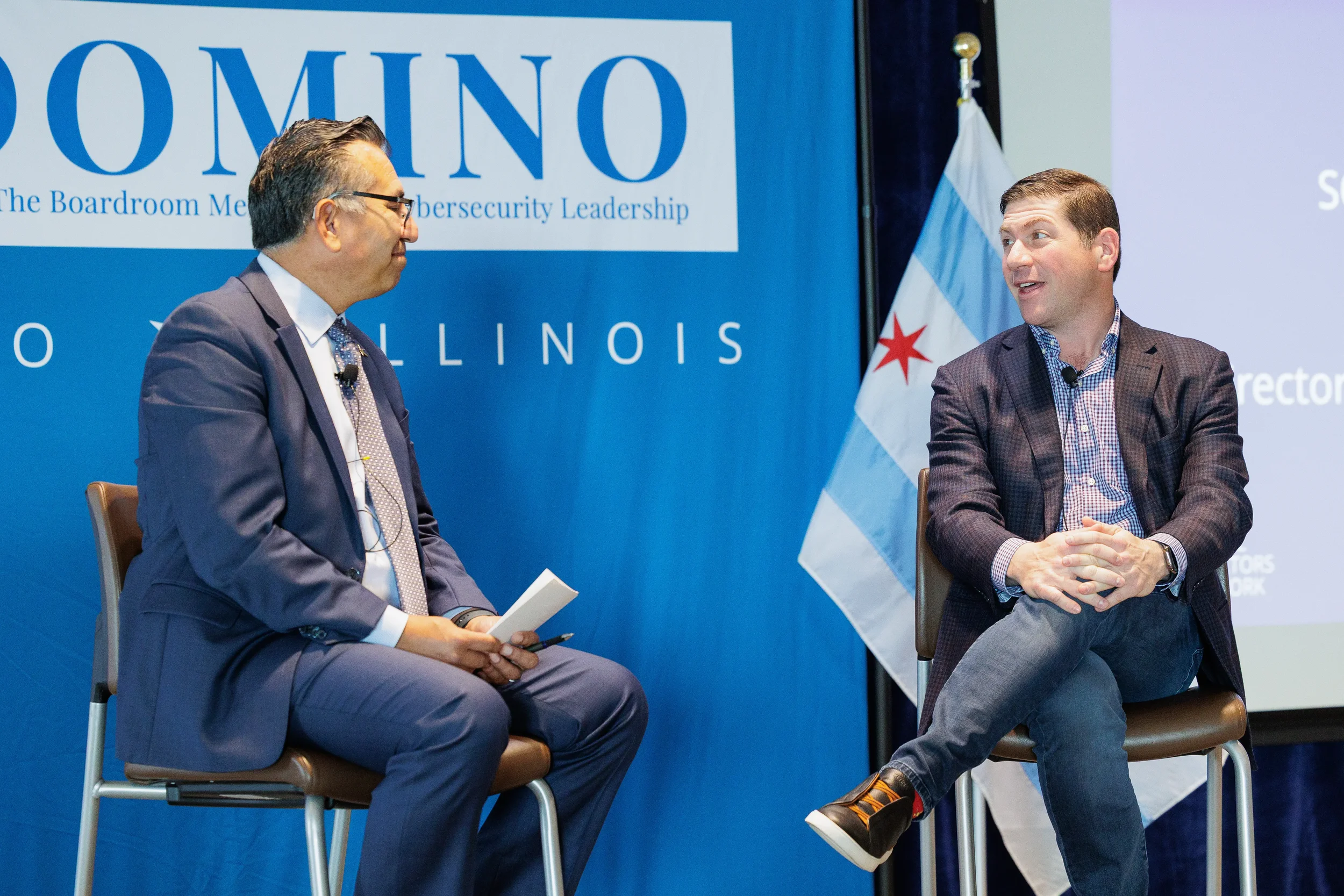 Two speakers seated for fireside chat in front of branded backdrop and Chicago flag at Chicago corporate event